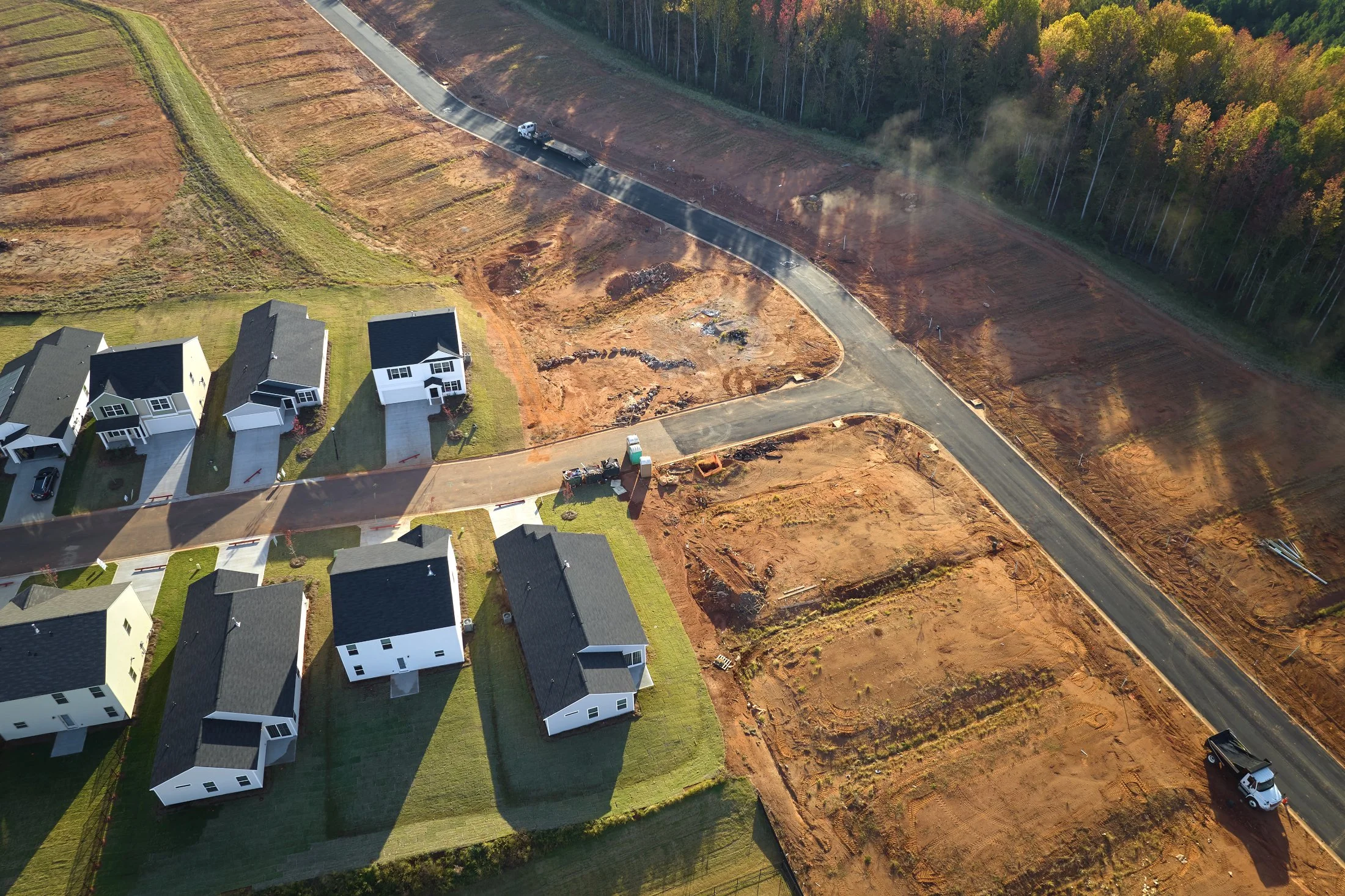 Aerial view of a residential neighborhood with several newly constructed houses and ongoing road construction, with some areas cleared and prepared for more development.