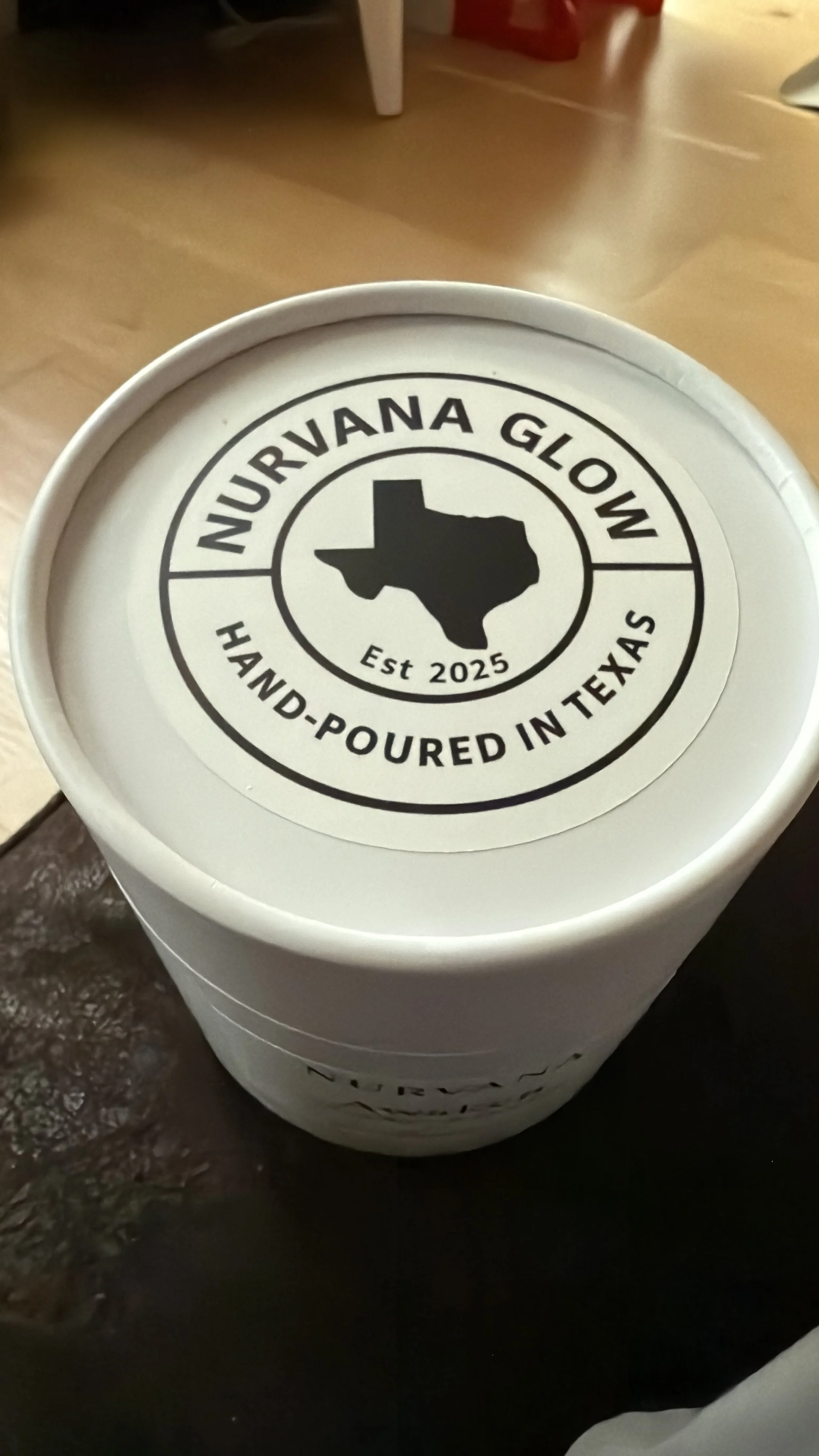A white container lid with a logo that reads 'NURVANA GLOW,' featuring a silhouette of Texas, and the text 'Hand-Poured in Texas' and 'Est 2025'.