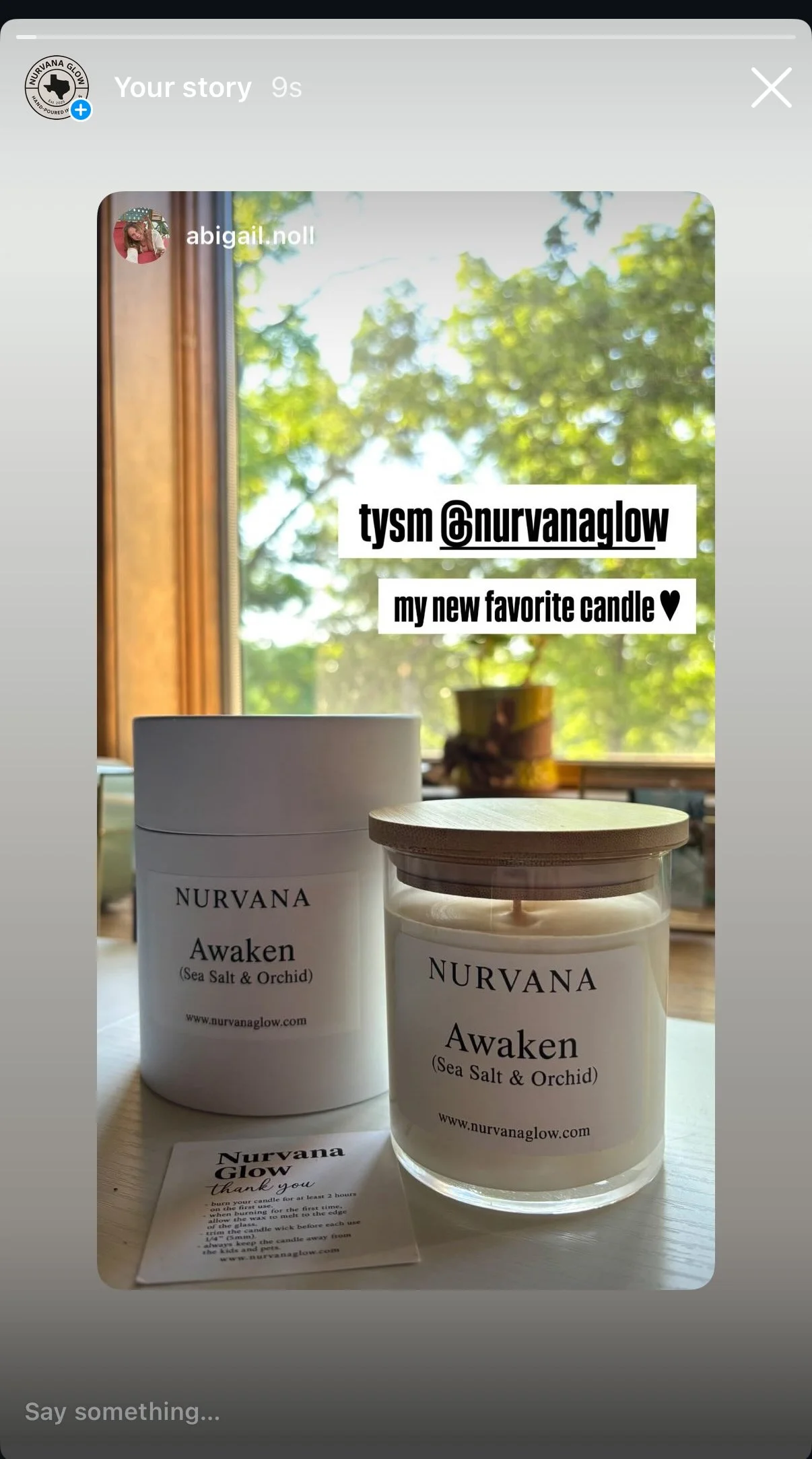 A photo of two Nurvana candle jars labeled "Awaken" with Sea Salt & Orchid scent, placed on a table near a window with a blurred green outdoor view. A small thank you note is in front of the candles.
