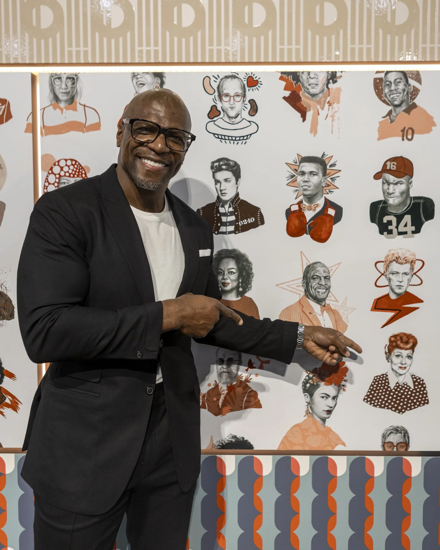 Terry Crews smiling and pointing to a portrait of Lucille Ball on the Iconographic wallcovering mural during a tradeshow exhibition, surrounded by illustrated cultural icons