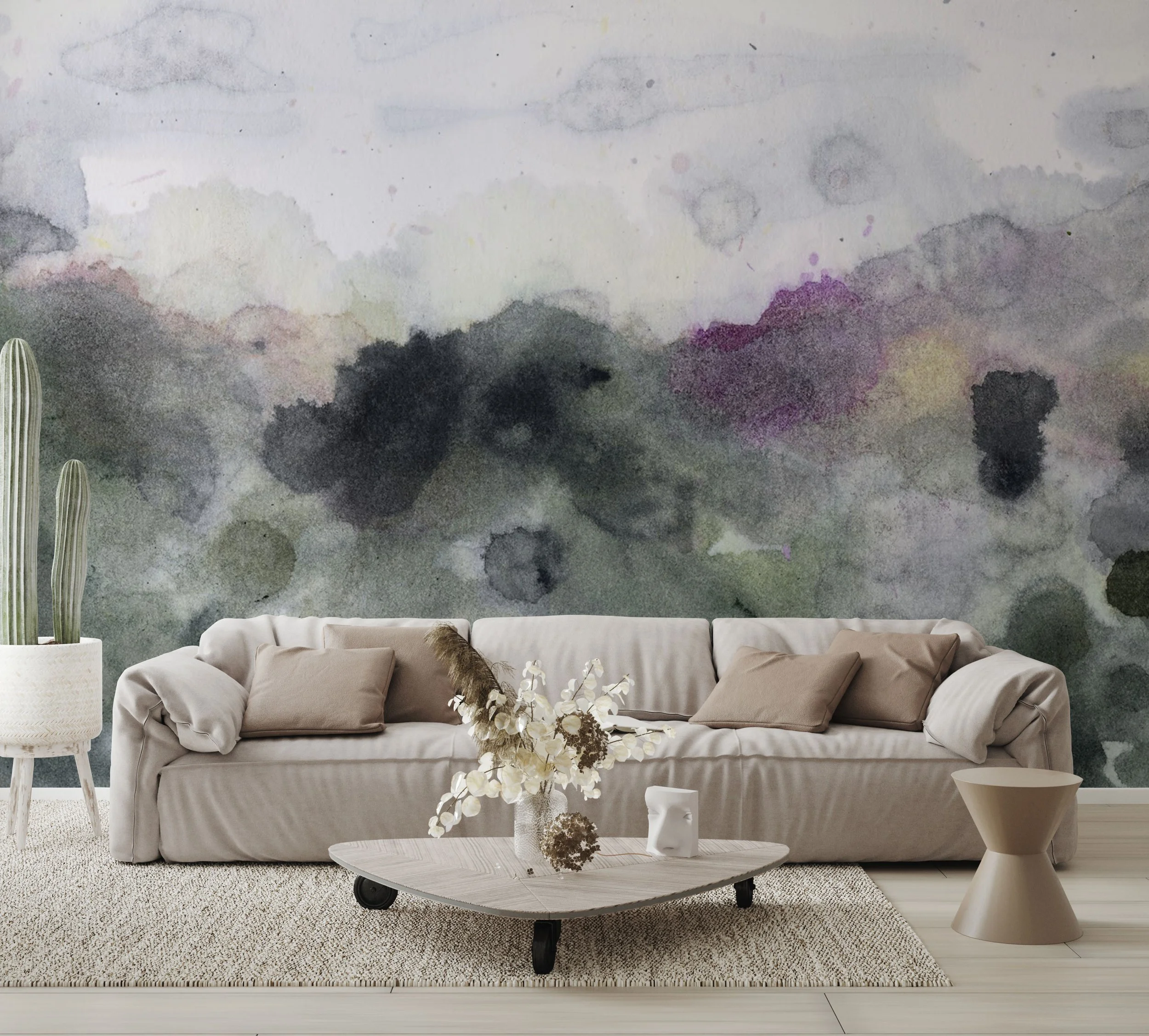 Watercolor-inspired mural in moody green, gray, and plum tones behind a modern beige sofa with neutral accents and sculptural decor.