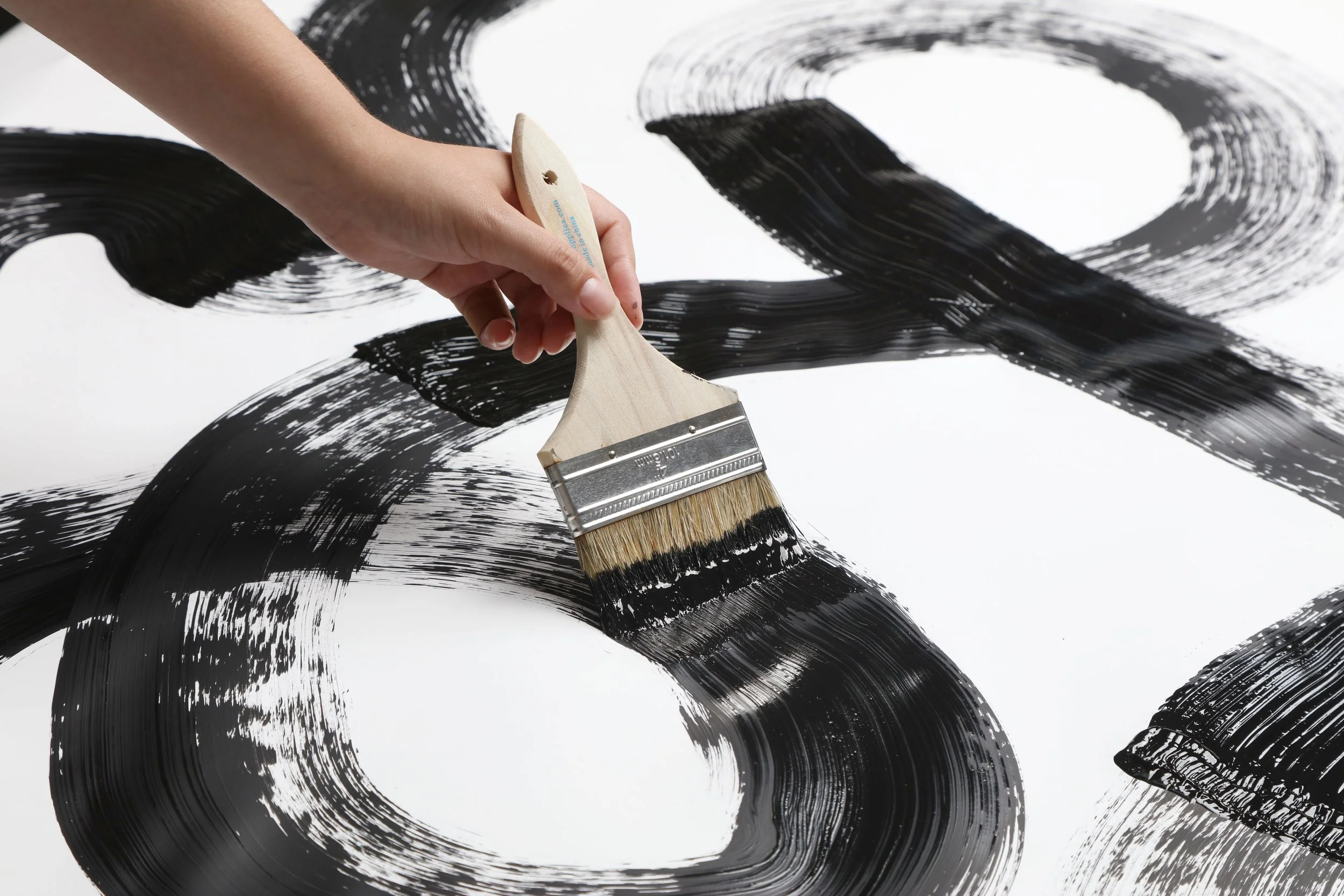 Close-up of a hand painting bold black brushstrokes on white paper for the Resonance collection