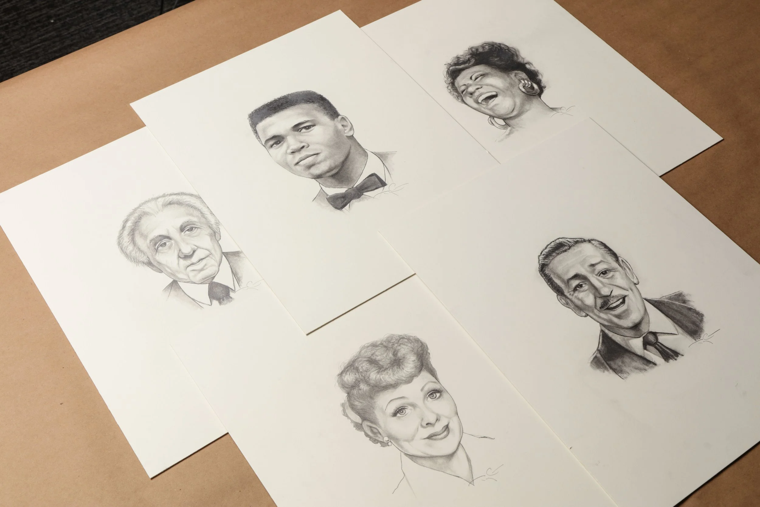 Graphite portrait sketches by Terry Crews featuring Lucille Ball, Muhammad Ali, Walt Disney, Aretha Franklin, Frank Lloyd Wright, and Albert Einstein, laid out on a work surface during the creation of the Iconographic collection.