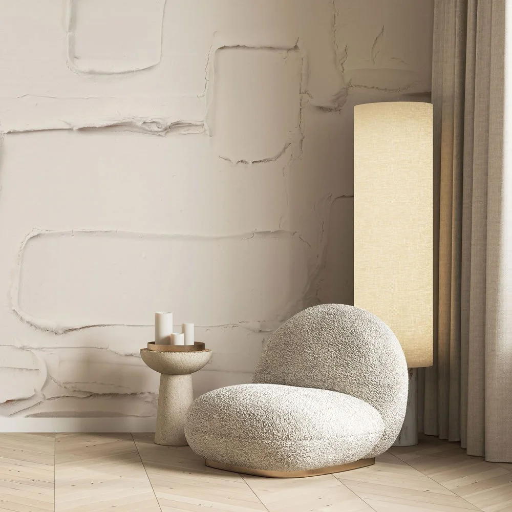 Softly textured plaster wallcovering in an eggshell tone, styled with a boucle lounge chair, sculptural candle pedestal, and warm ambient lighting in a serene interior corner.