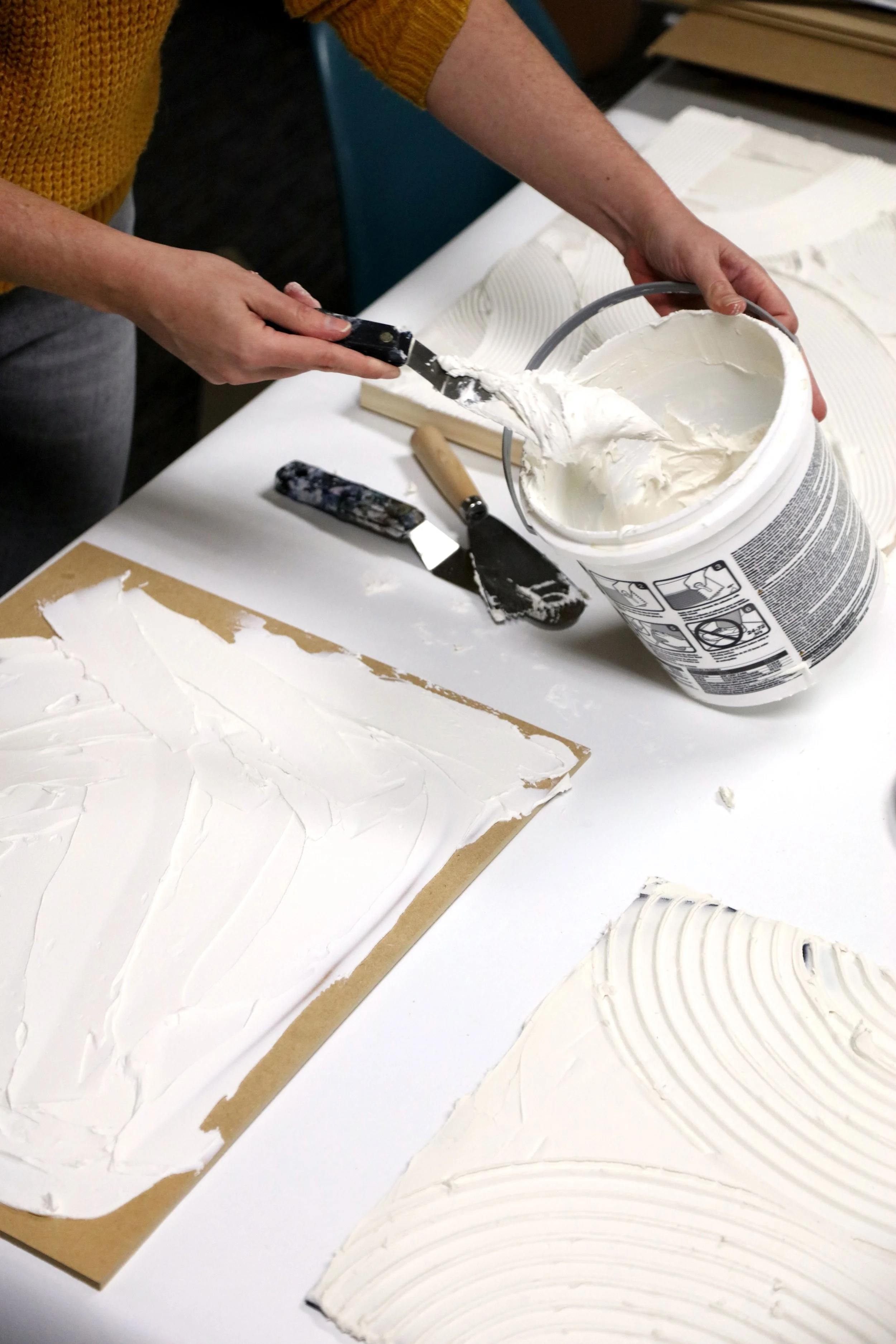 Artist spreading sculptural white plaster onto board using a palette knife during the development of textured wallcovering samples.