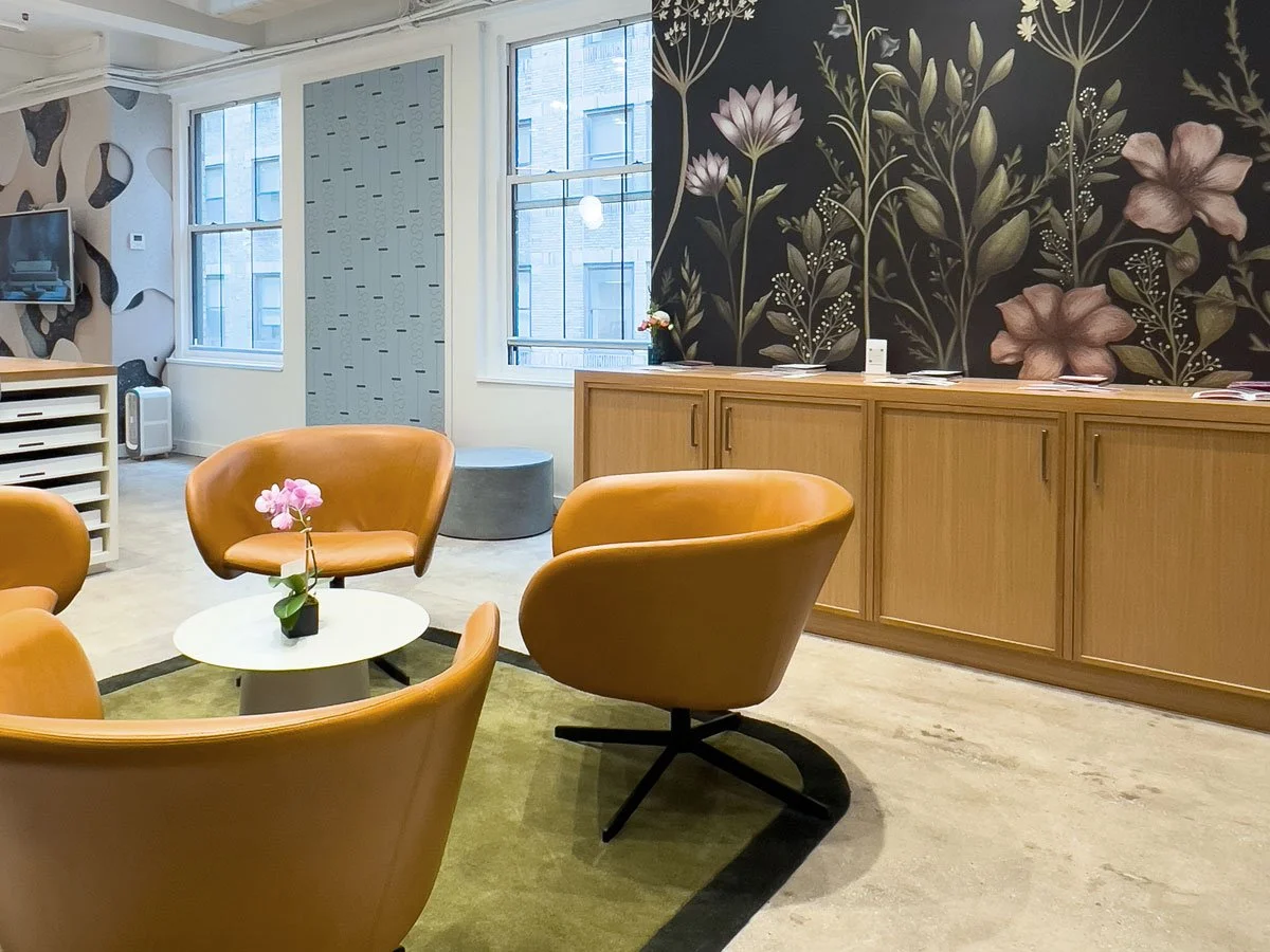 Modern office lounge space with custom botanical wallcovering and leather chairs.