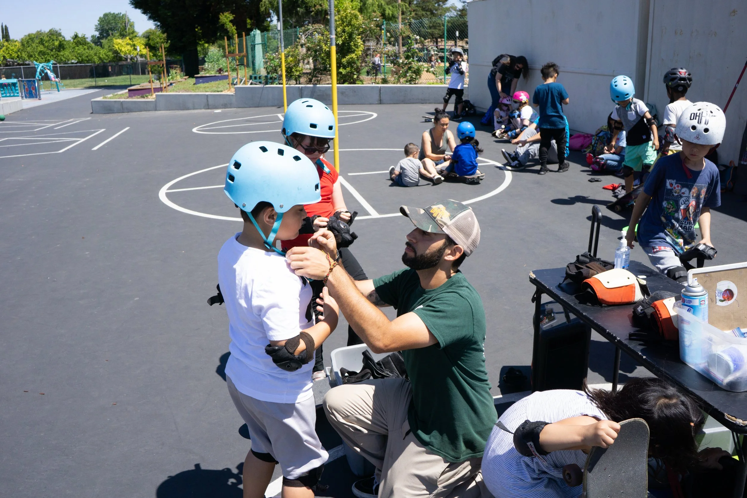 Diego Flores is squatting down to help a young skater adjust his helmet.