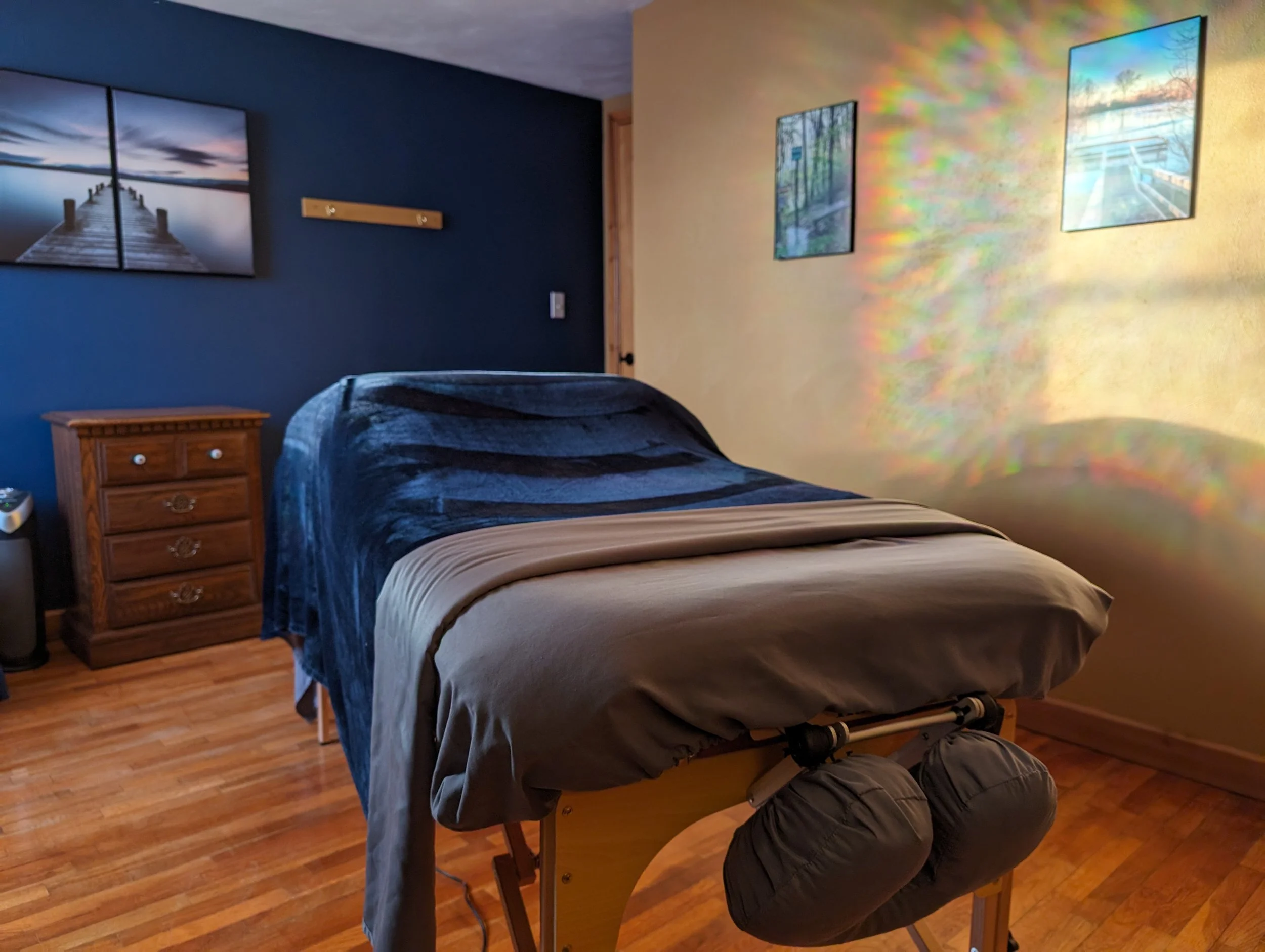 Massage table in a room with blue and yellow walls, artwork, and wooden furniture.