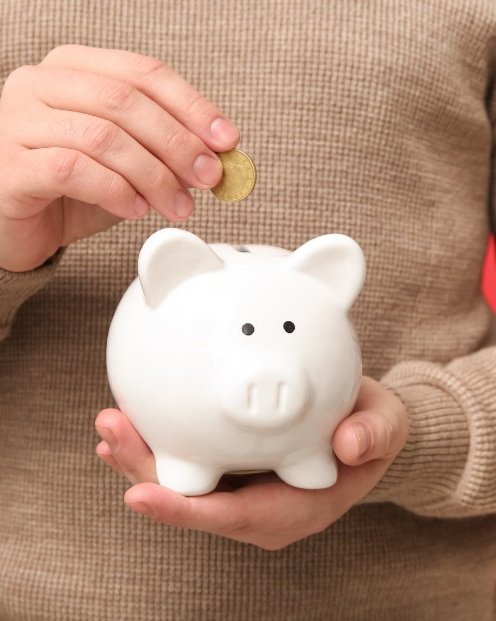 Person placing a gold coin into a white piggy bank.