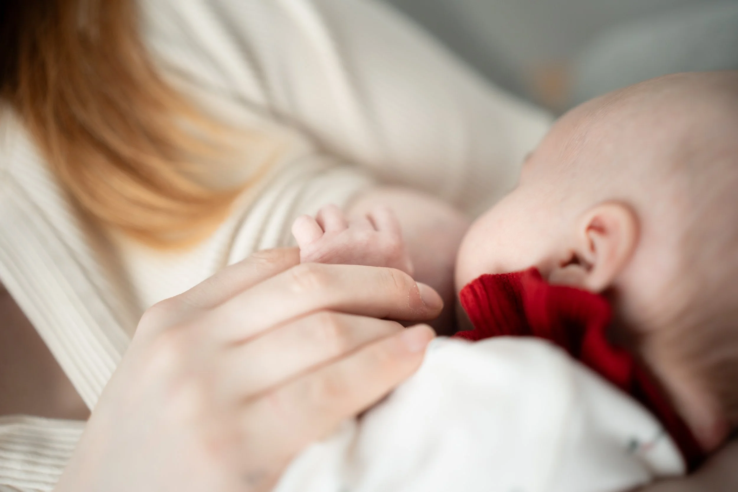 A person breastfeeding an infant, holding the baby's hand gently. Motherhood photography, lifestyle, Wasilla AK.