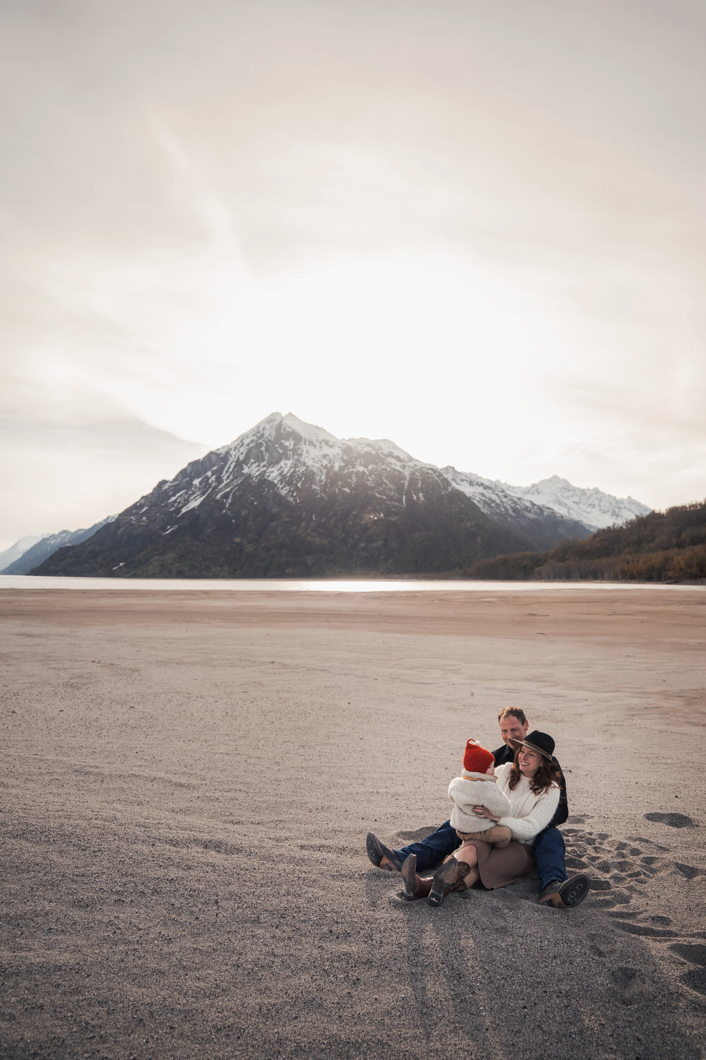 A happy family sitting on the sandy beach with snow-capped mountains in the background, enjoying each other's company. Adventurous Alaska Photos Anchorage. Airplane Expedition.