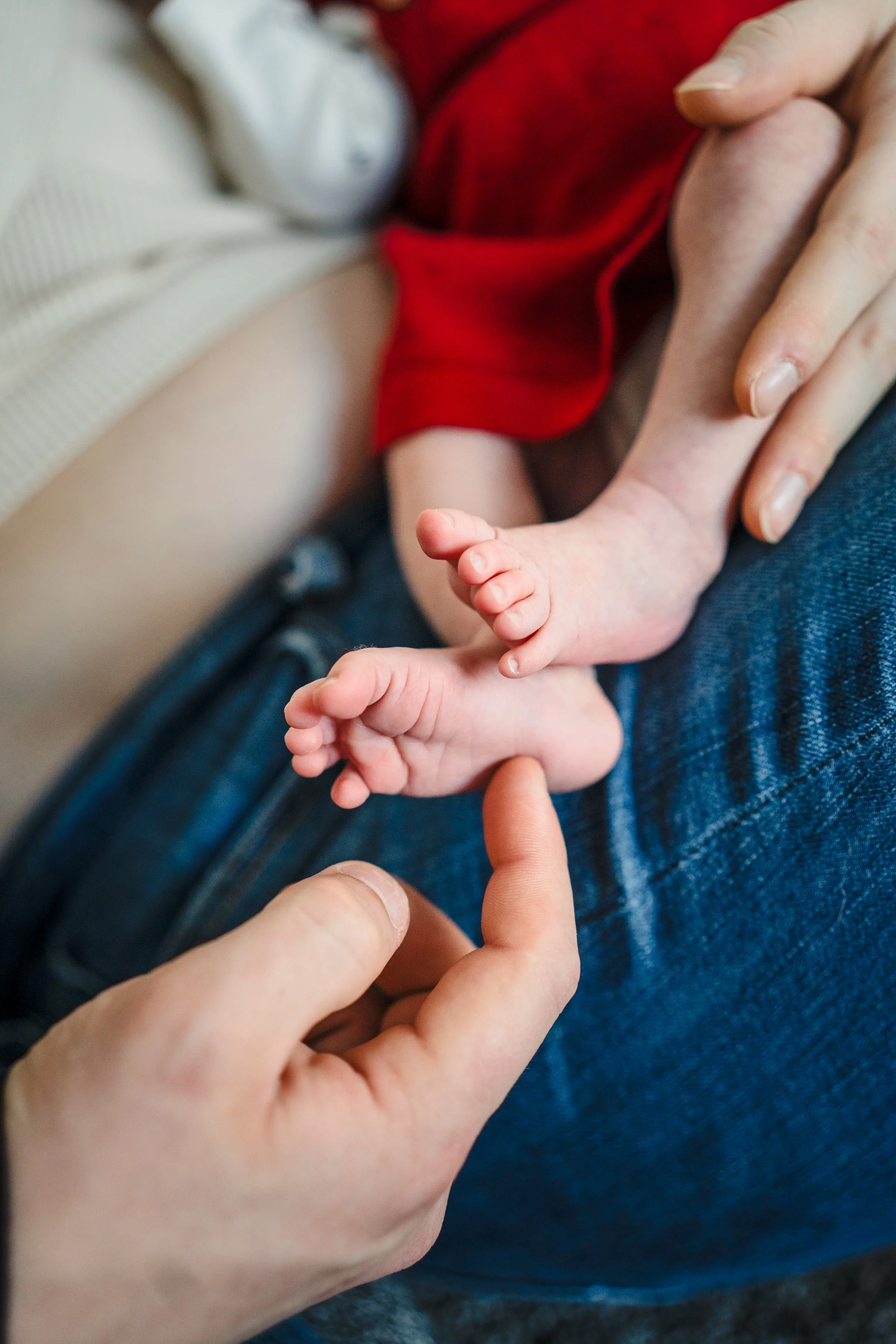 Close-up of a parent's hand holding a small baby's hand, with the baby's tiny hand pressing against the parent's finger. The scene depicts tenderness and connection. In home newborn session. Anchorage AK.