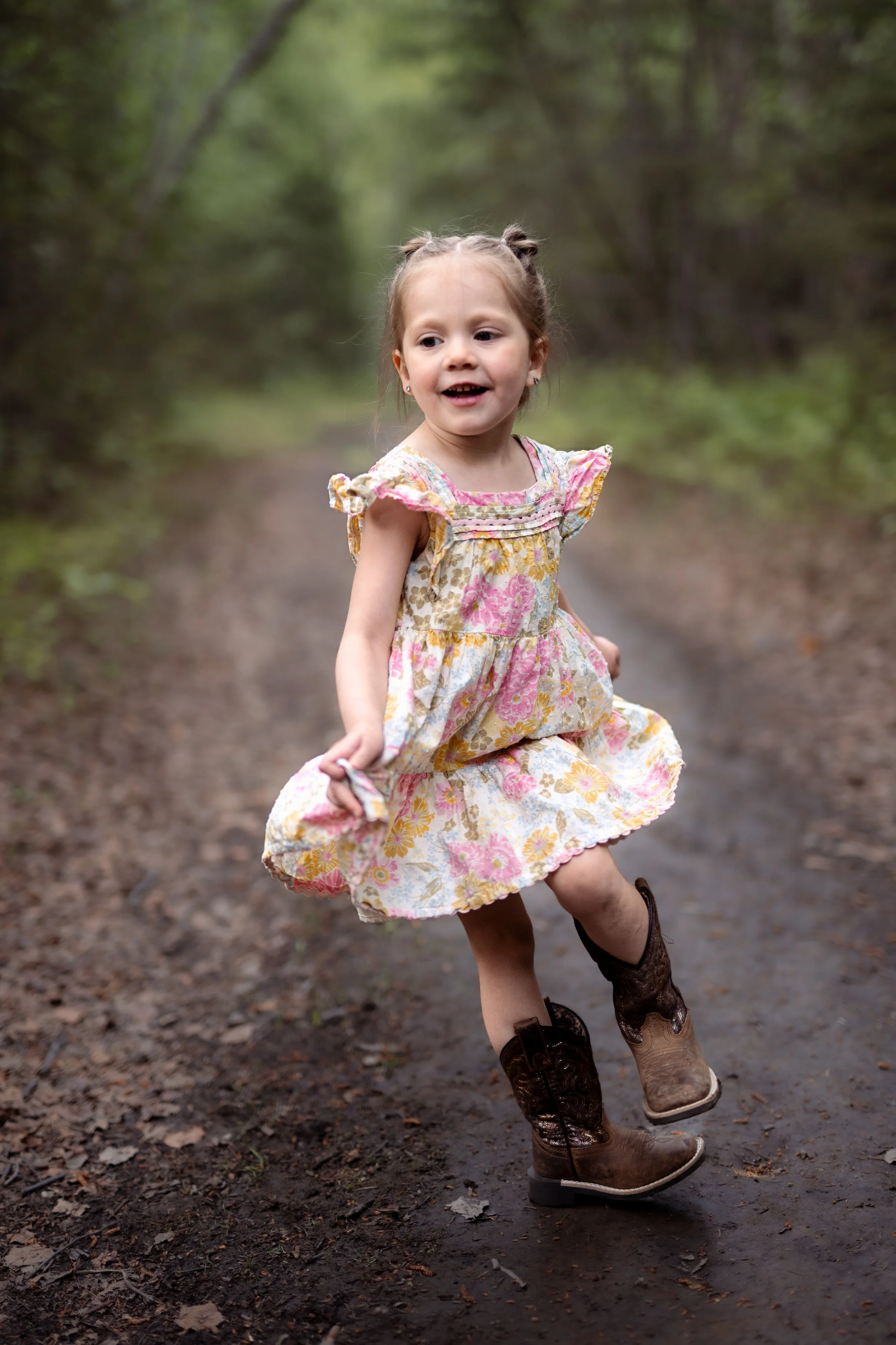 A young girl with a floral dress and cowboy boots running on a forest trail. Natural Childhood portraits. Girdwood, Alaska Family Photography.