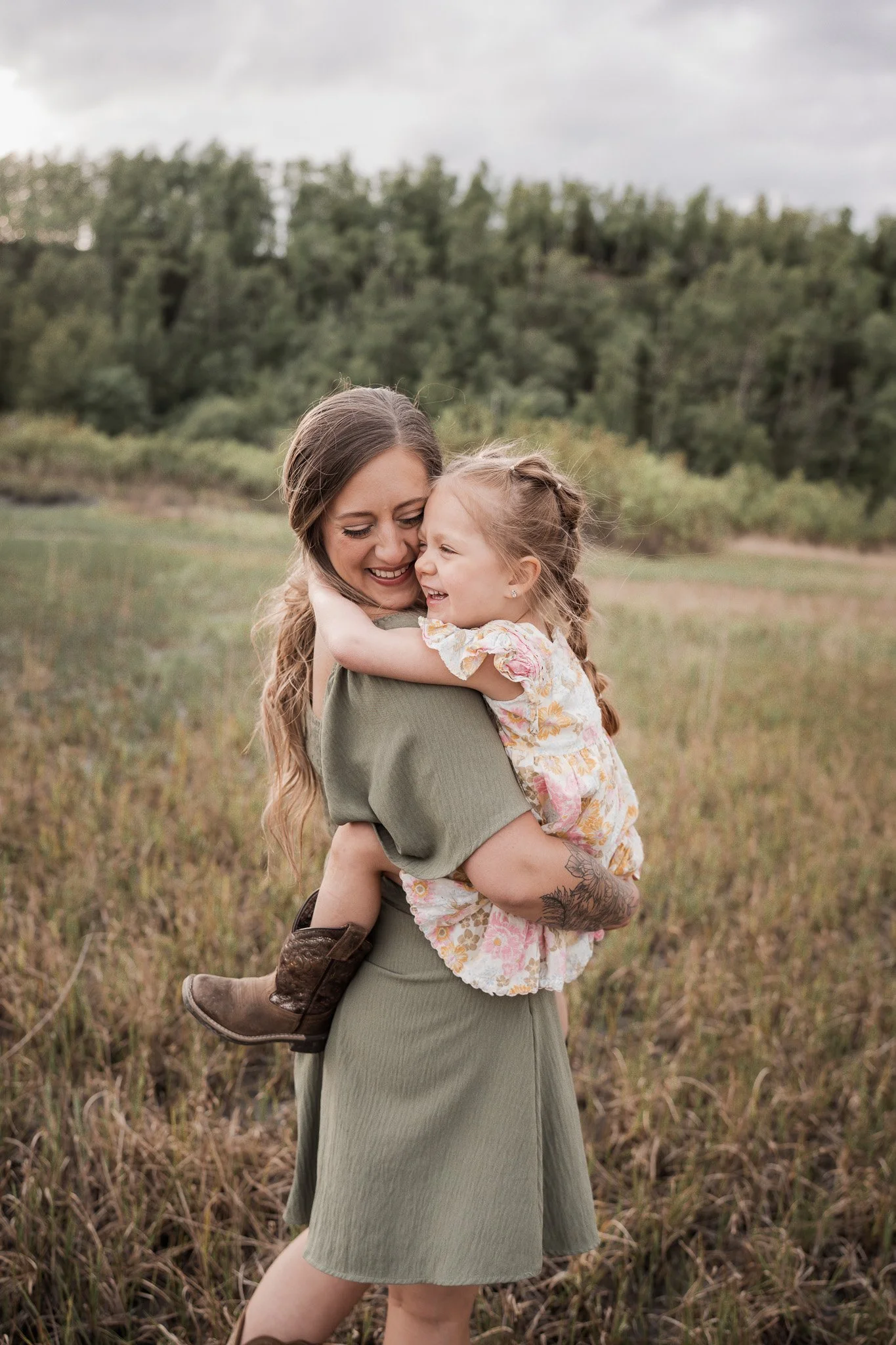 A woman holding a young girl in an outdoor field during daytime, both smiling and hugging. Palmer Hay flats photo shoot.