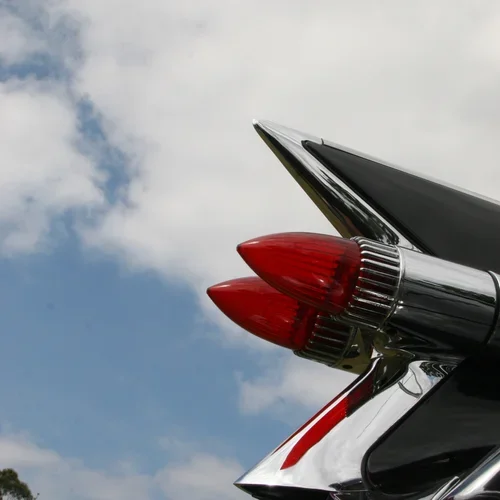 Close-up of a vintage car's tail fins with red taillights against a cloudy sky.