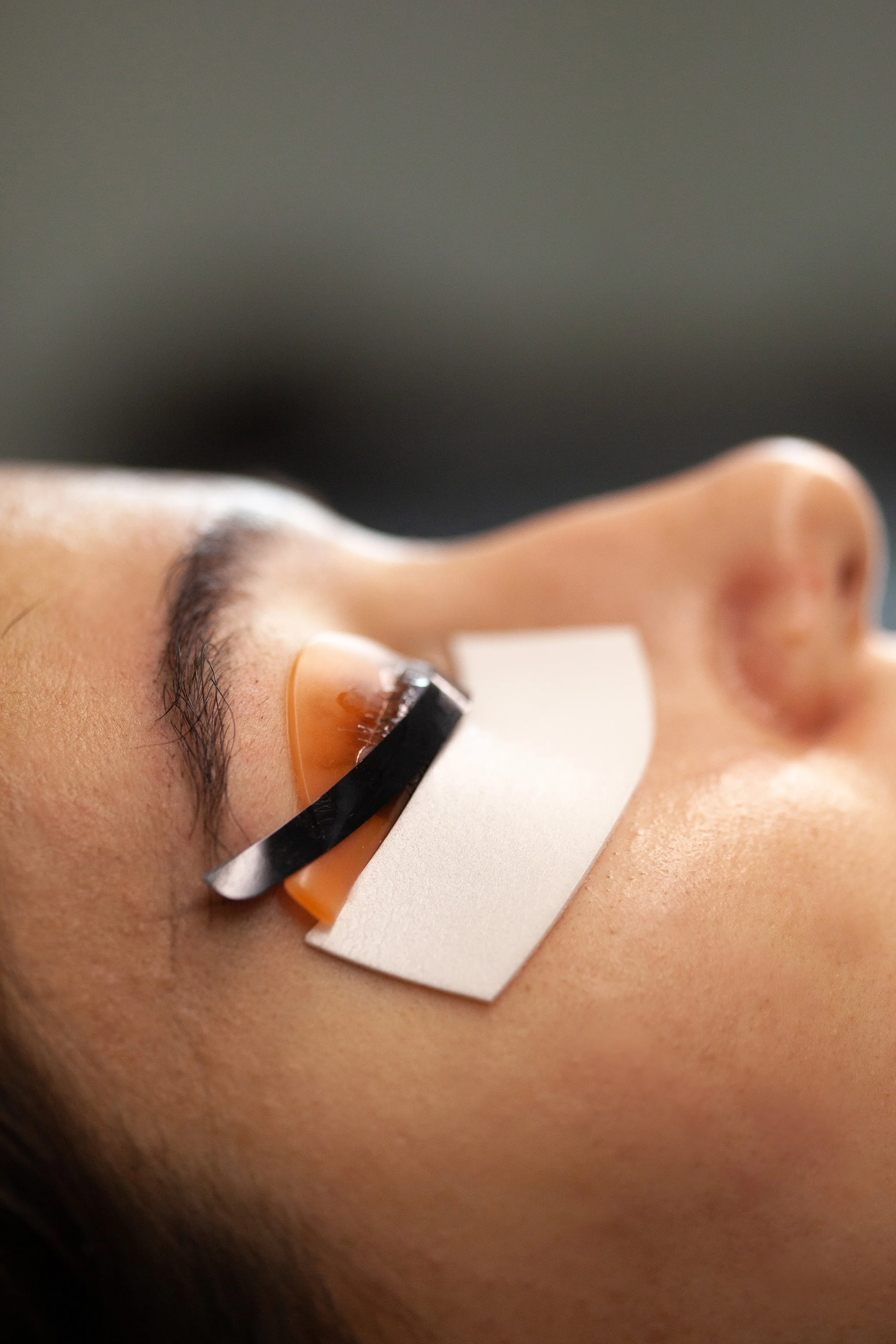 Close-up of a person's eye with a medical eye patch covering the lower eyelid, secured with tape, likely during an eye procedure or treatment. Dbeaute studio. Lash & Brow Lift. Powder brows. Makeup art. Dbeaute studio Zagreb. Beauty studio. Puder obr