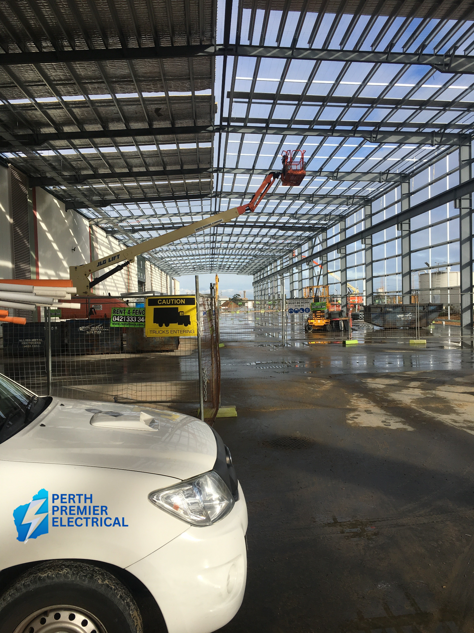 Construction site inside a building with glass walls and roof, machinery, and safety signs.