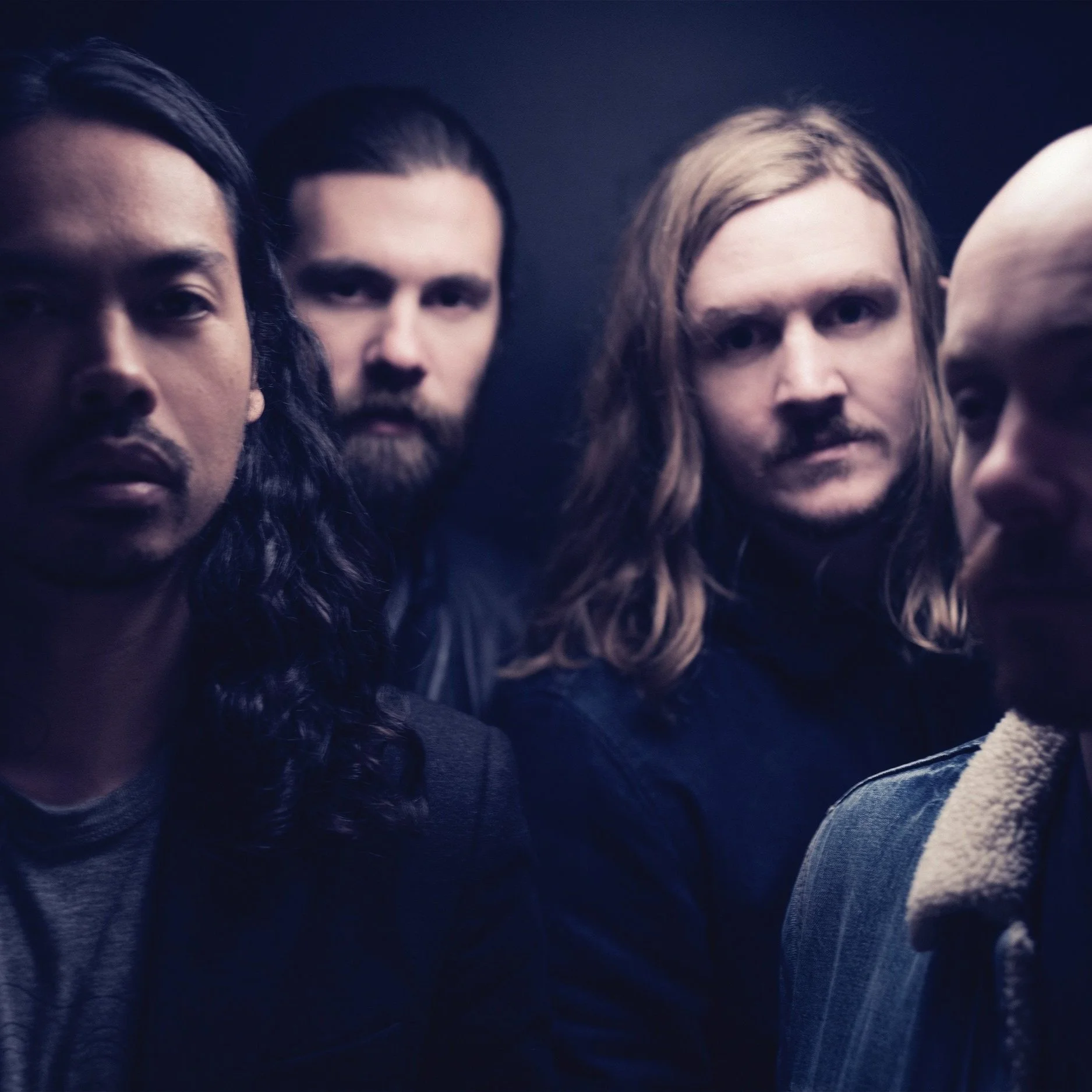 Four men with long hair and beards, posing in a dark setting.