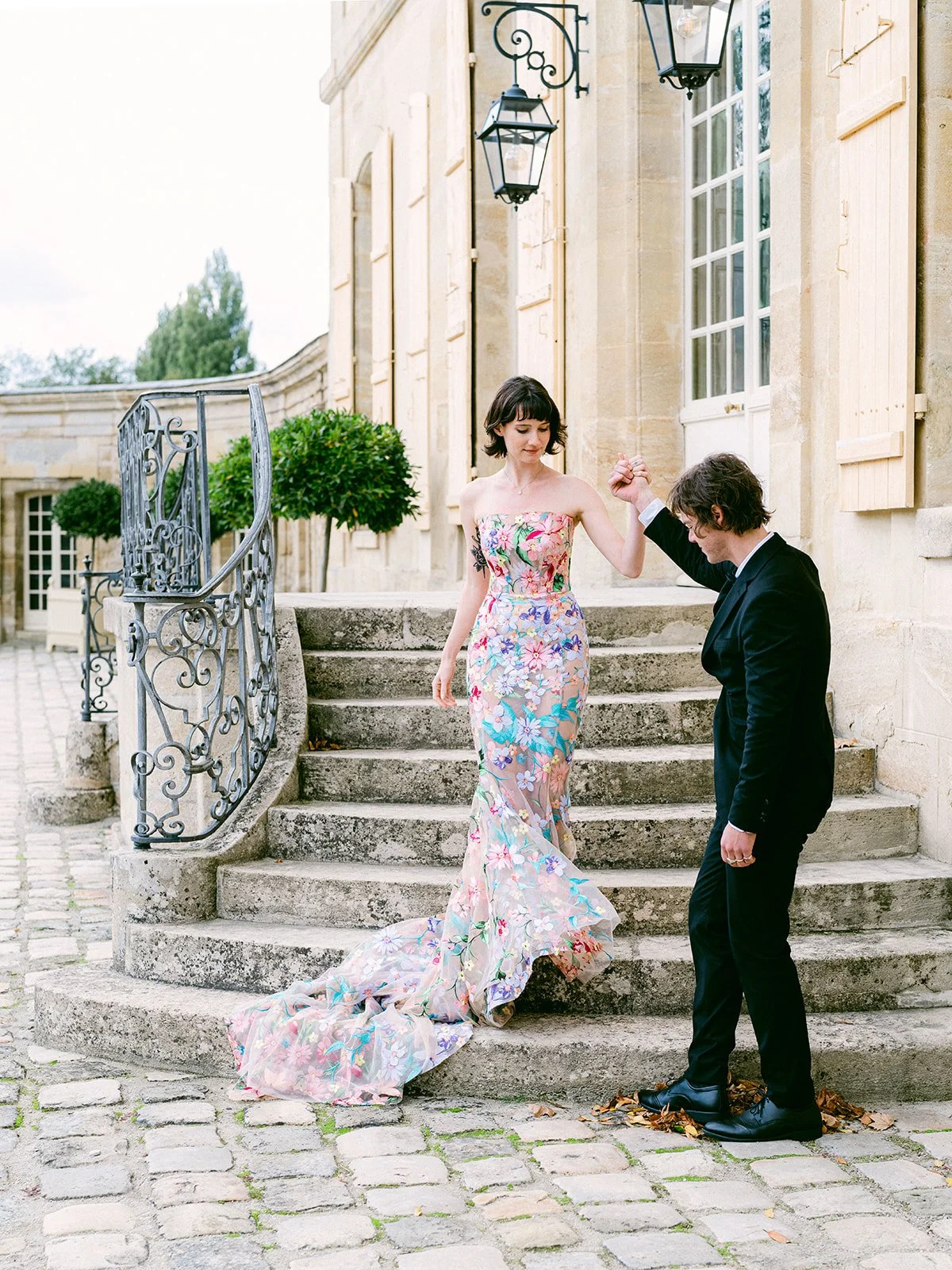 Four young adults dressed in formal attire standing outdoors on grass during evening, with trees and a clear sky in the background.