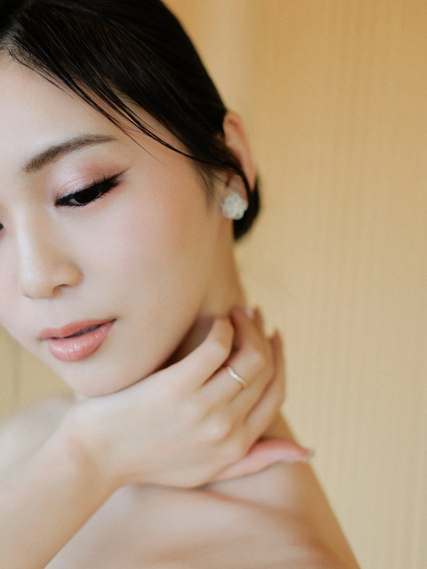 A woman with dark hair, wearing makeup, partially obscured by a branch with pink flowers.
