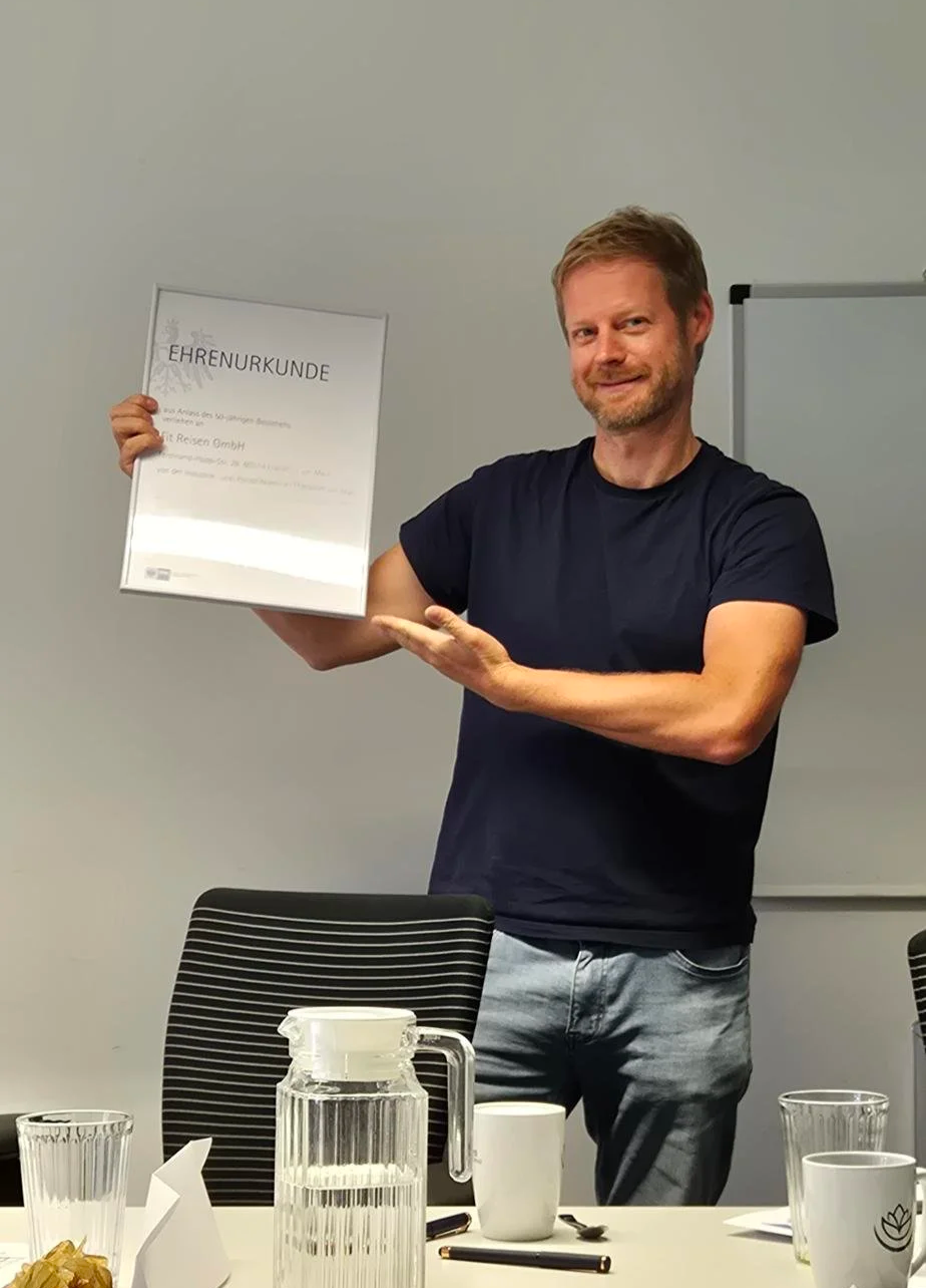 Nils holds a certificate in his hand and stands at a conference table.