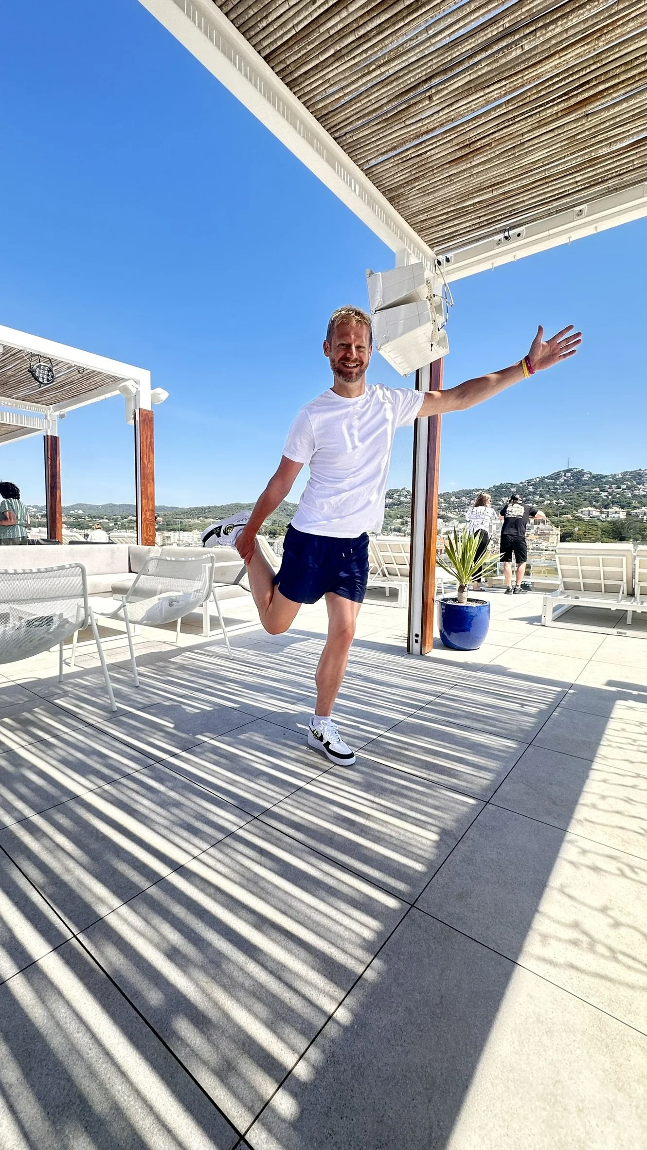 Nils does a yoga stretch on the roof terrace during the seminar trip 2025 in bright sunshine, with a blue sky and a city in the background.