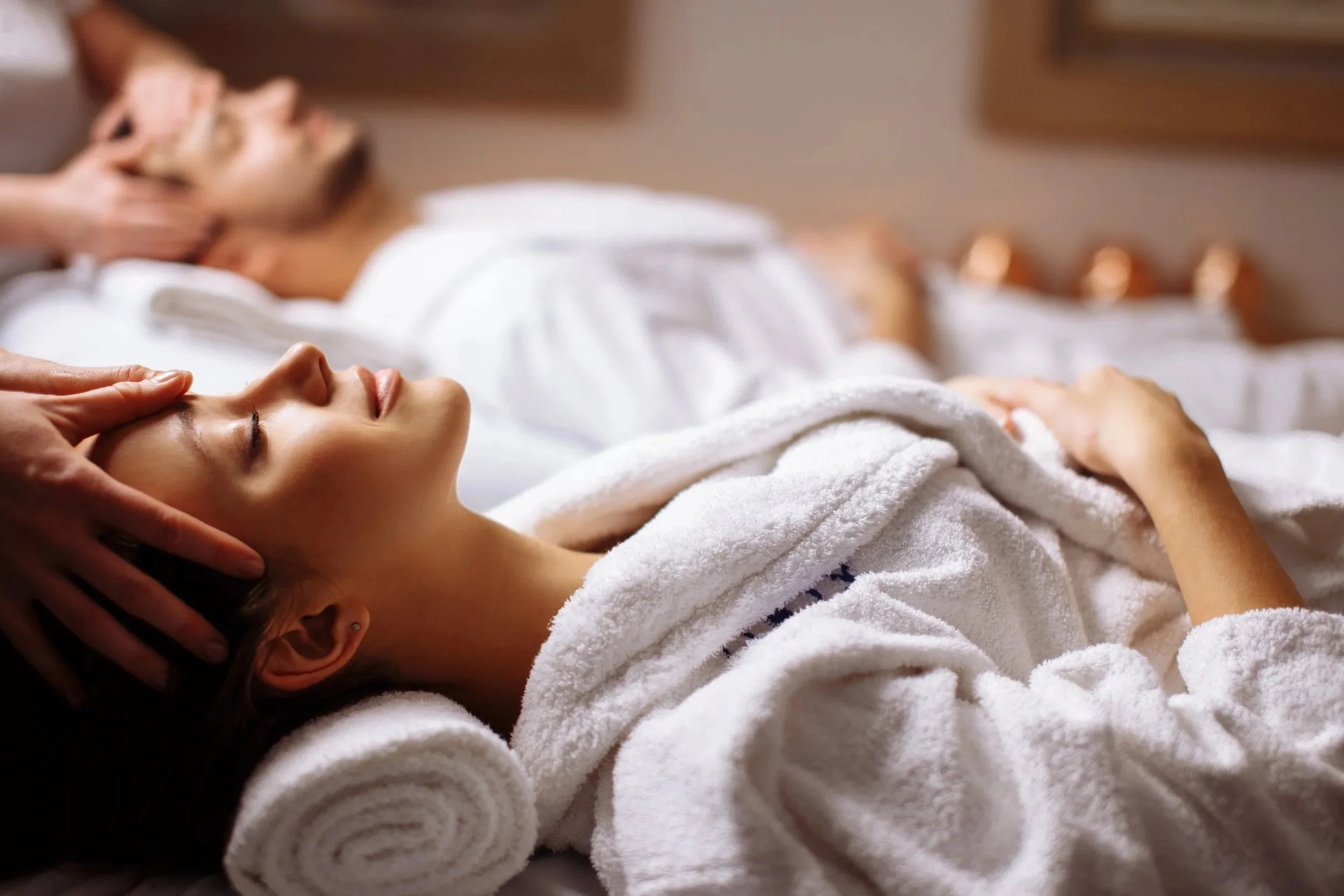 People enjoying a massage in a spa or wellness center lie on loungers covered with white towels.