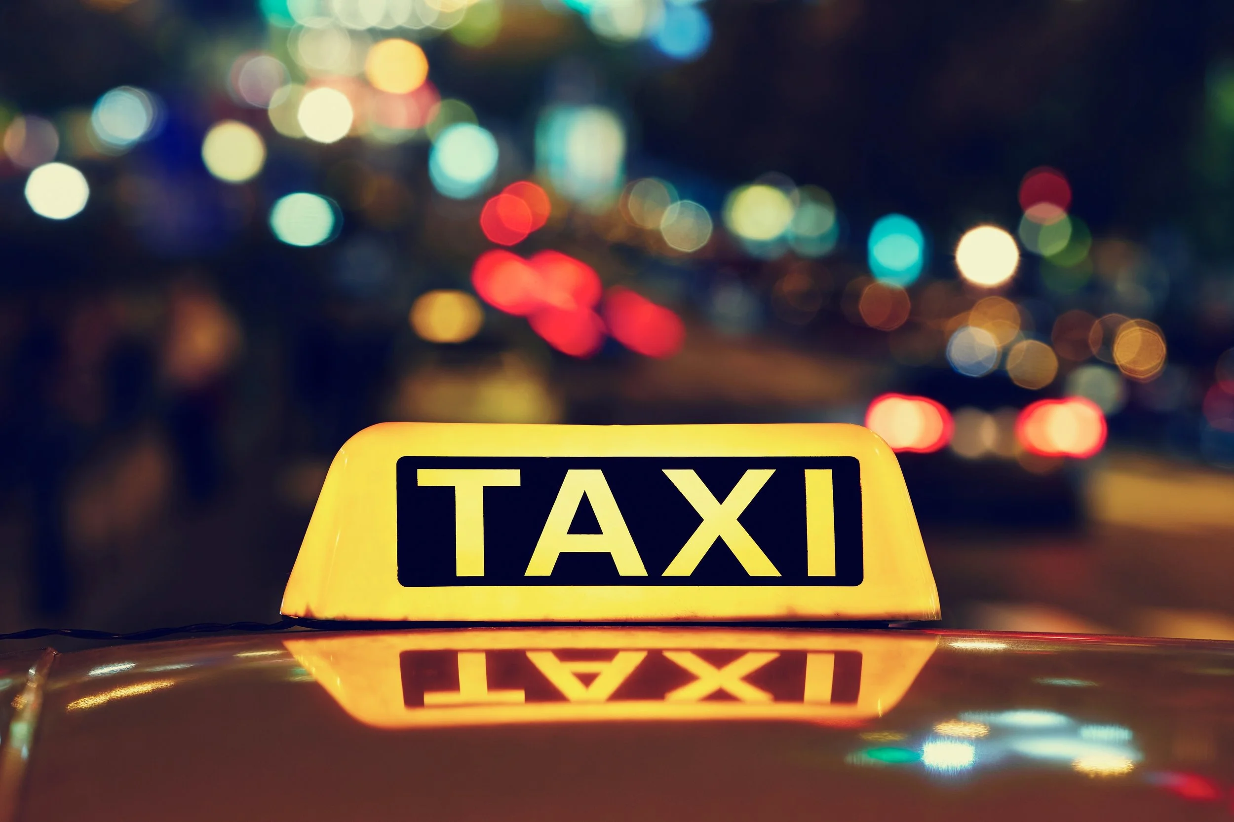 Leuchtendes Taxi-Schild bei Nacht mit bunten Stadtlichtern im Hintergrund.