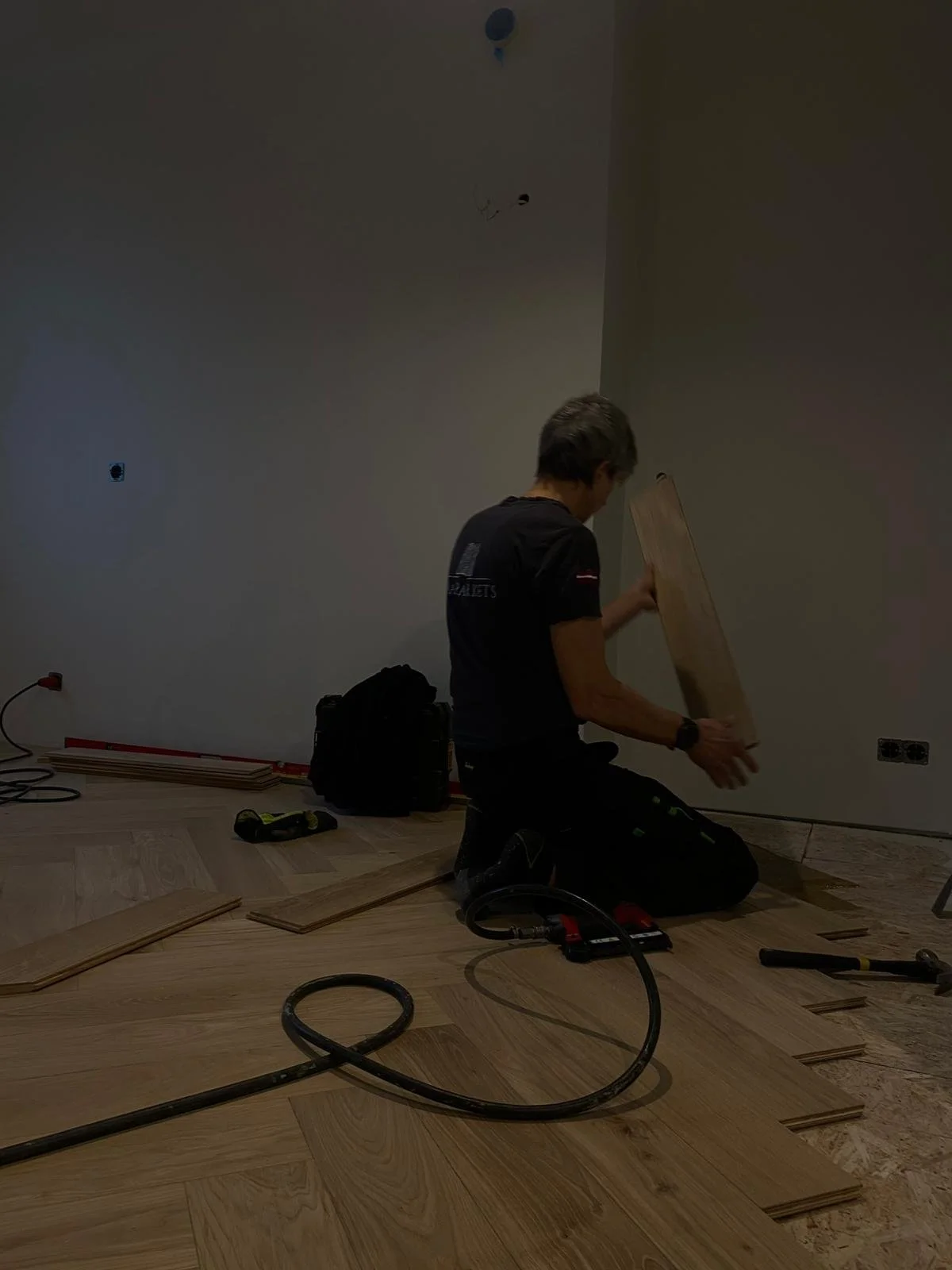 A person installing hardwood flooring in a room, kneeling on the floor with tools around.
