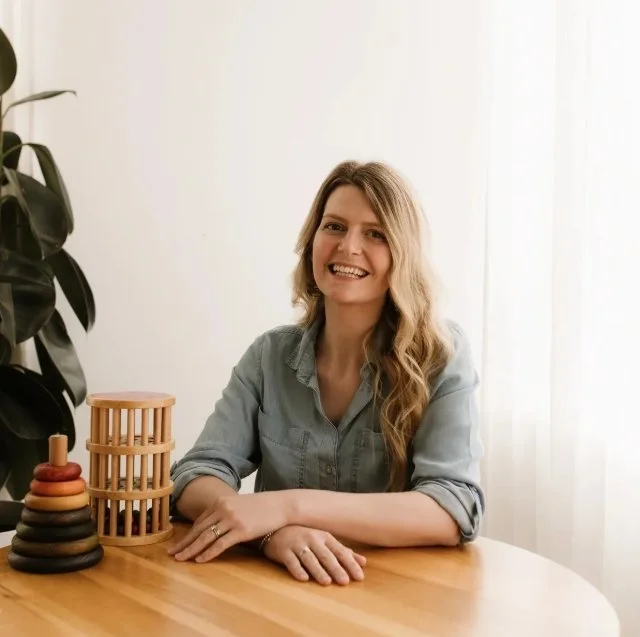 Female speech pathologist smiling at the camera wearing blue blouse, child building blocks next to her
