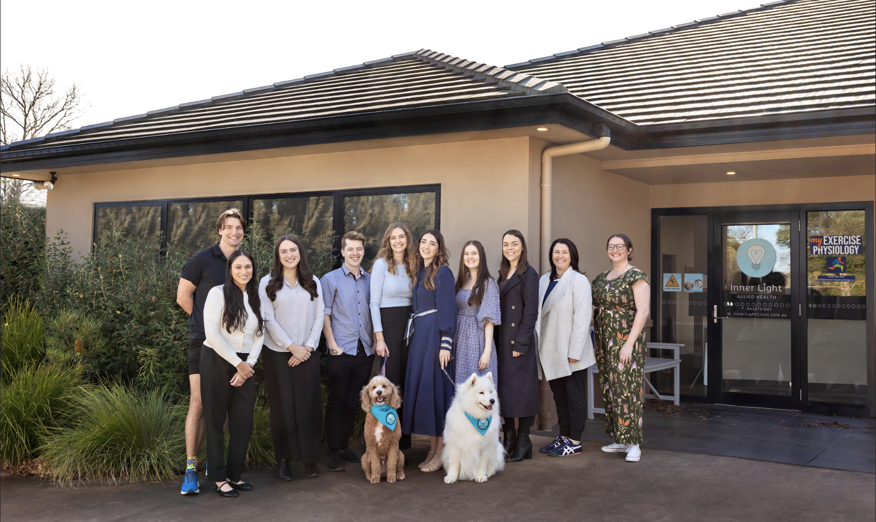 Group of eleven people standing outside a clinic, two dogs, and various signs on the glass door and window.