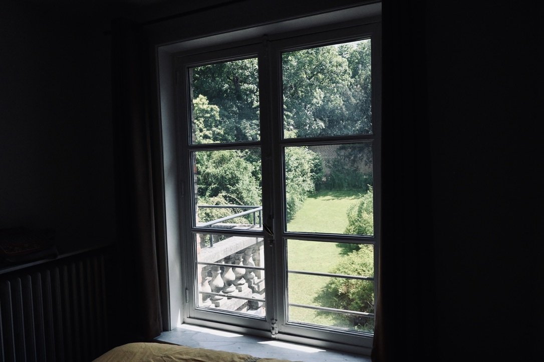 Interior view of a room with a window looking out onto a lush green garden with trees and grass