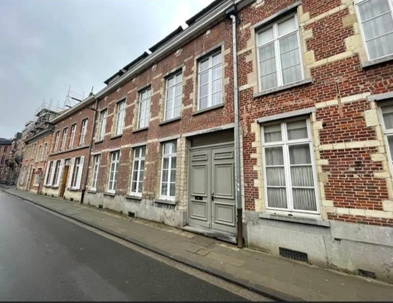 A row of brick townhouses with white-framed windows, a grey door, and a narrow sidewalk along a paved street under an overcast sky.