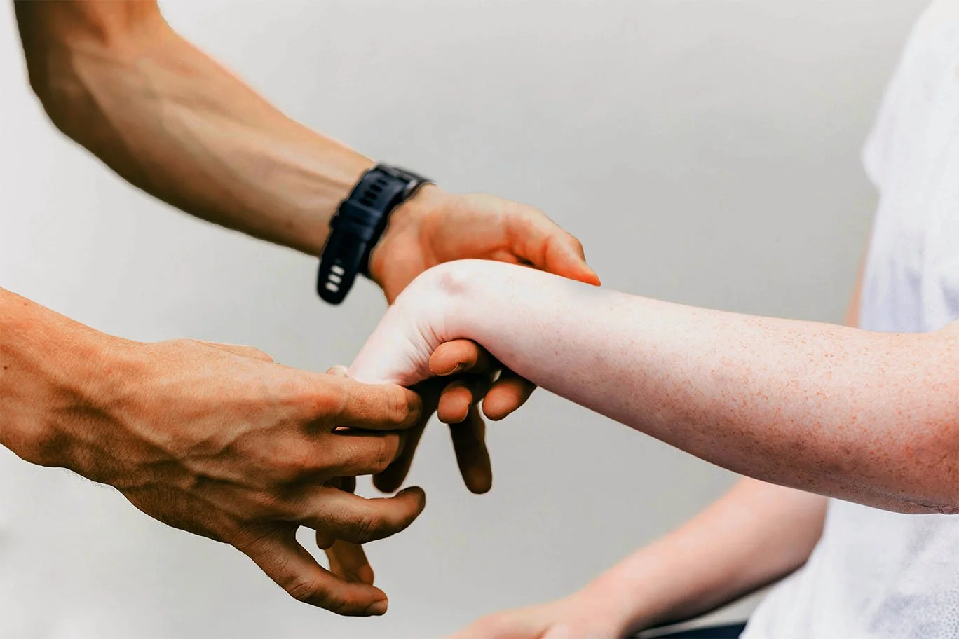 A person with a black wristwatch holding the hand of a child with freckled arm in a supportive gesture.