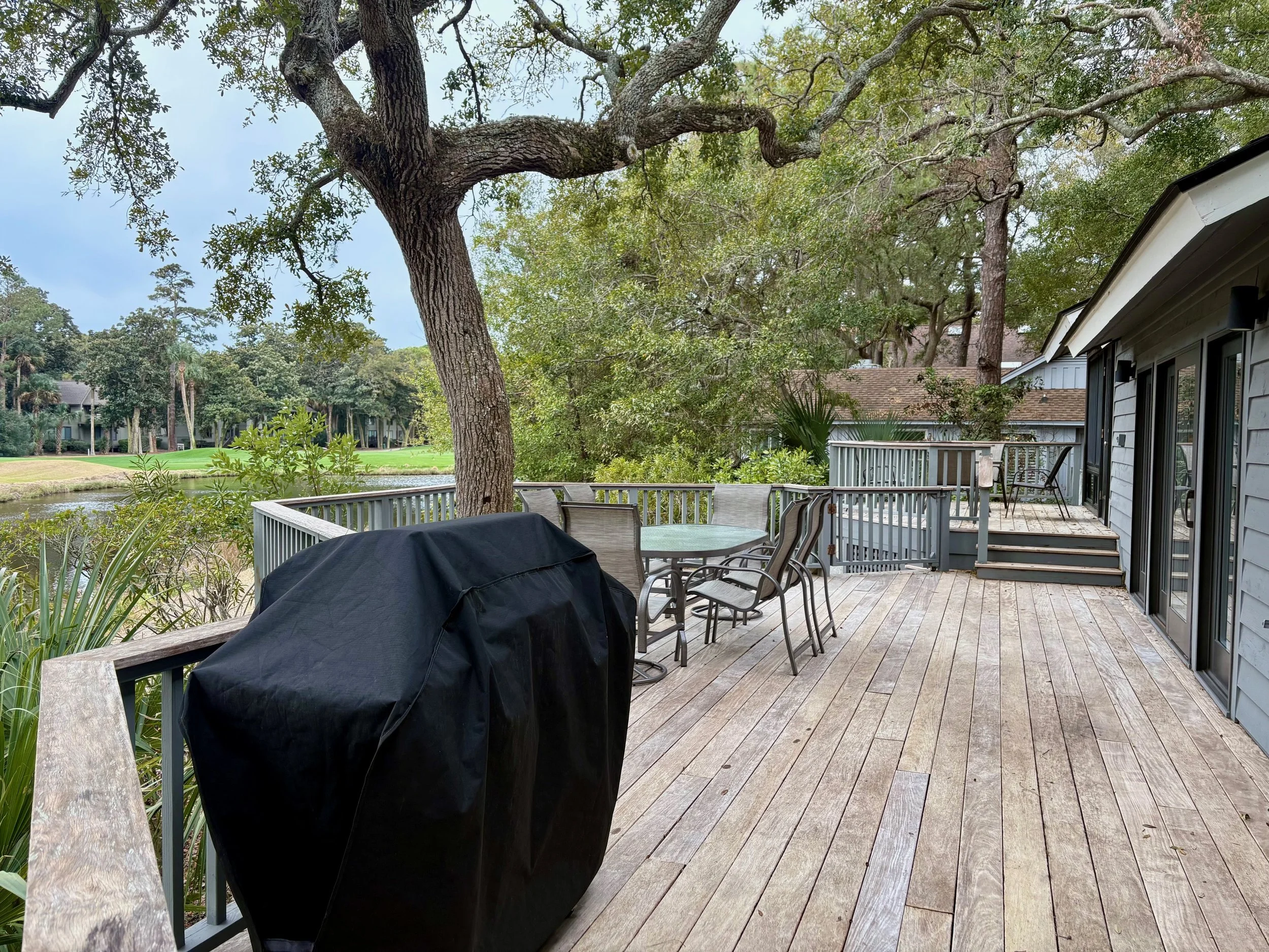 Wooden deck with outdoor furniture, a grill covered with a black cover, and mature trees with lush green foliage.