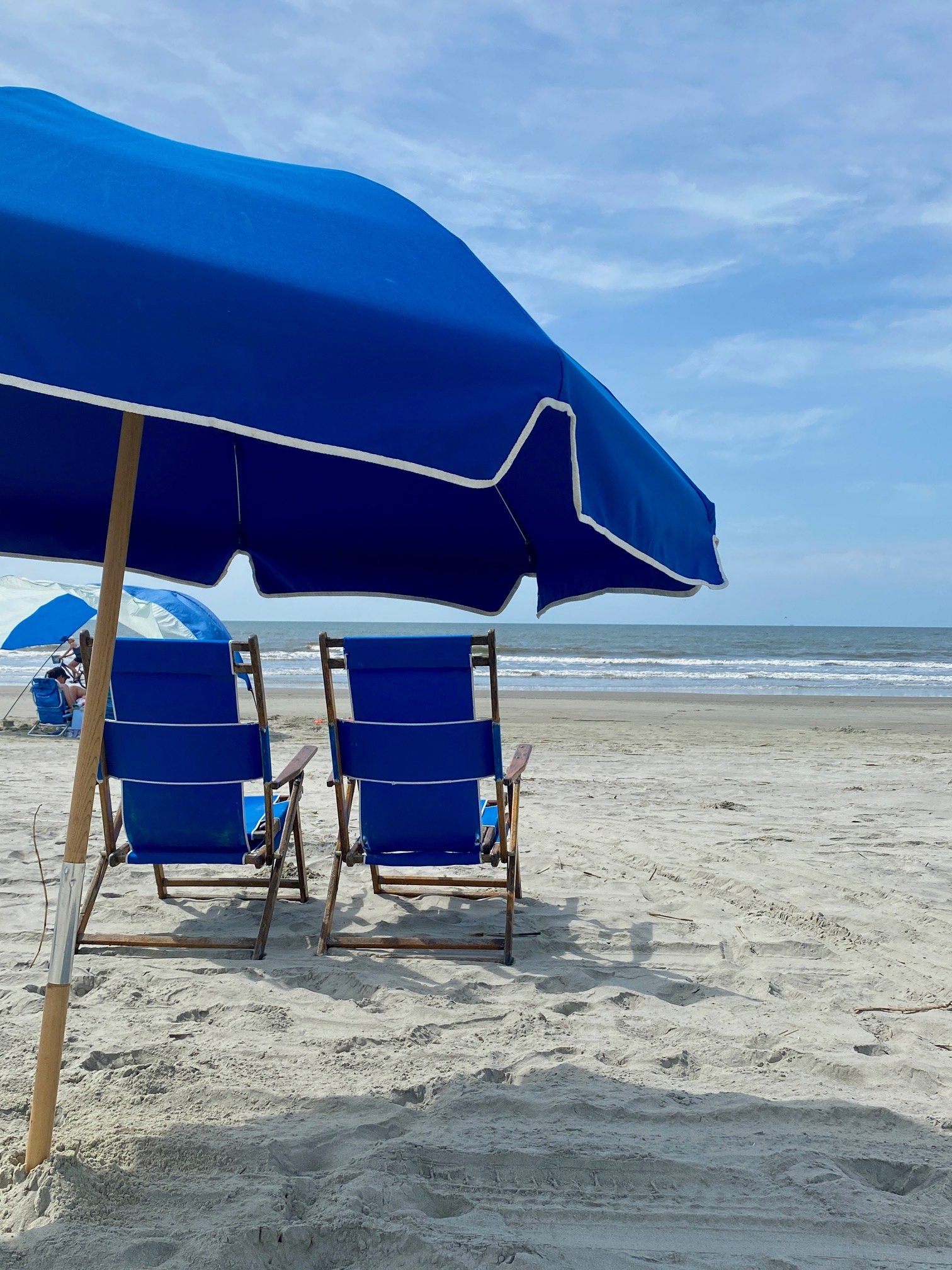 Two blue beach chairs under a blue beach umbrella on Kiawah Island facing the ocean.