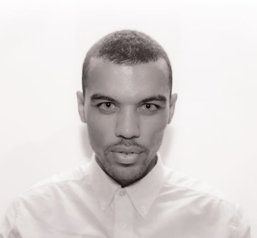 Black and white portrait of a young man with short hair, wearing a collared shirt, looking directly at the camera against a plain background.