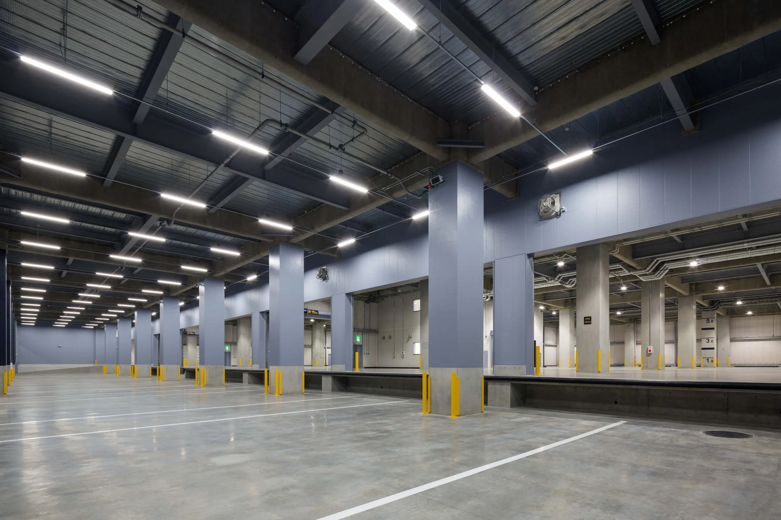 Empty indoor parking garage with yellow safety posts, gray columns, bright overhead lighting, and a smooth concrete floor.