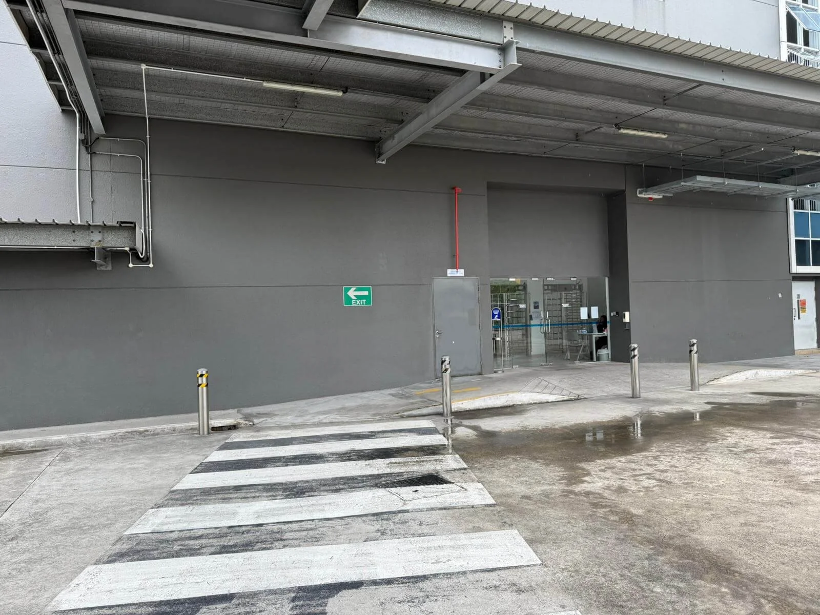 Empty parking lot with a pedestrian crosswalk, gray building wall, glass doors, an exit sign, and metal poles.