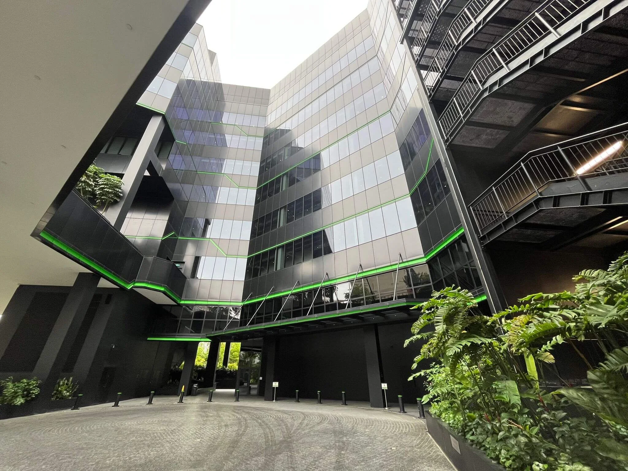 Modern multi-story office building with glass facade, surrounded by greenery and an open courtyard.