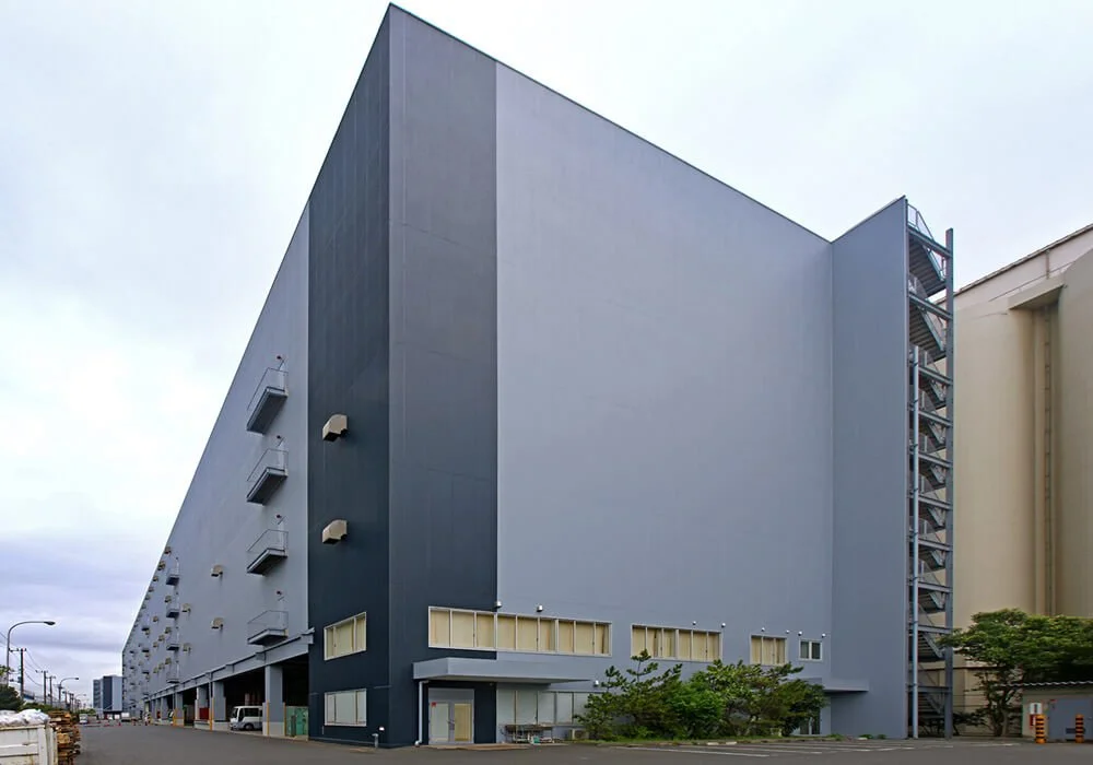 Large modern industrial building with multiple small windows and fire escape stairs on the side.