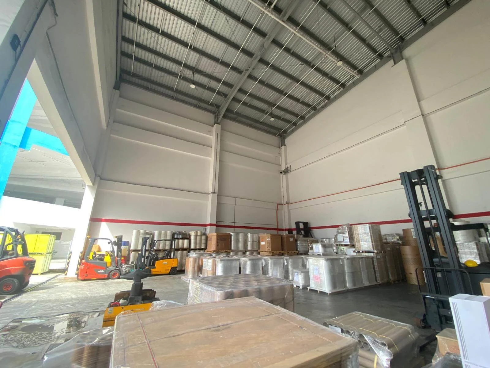 Interior of a warehouse with stacked pallets, boxes, and forklifts.