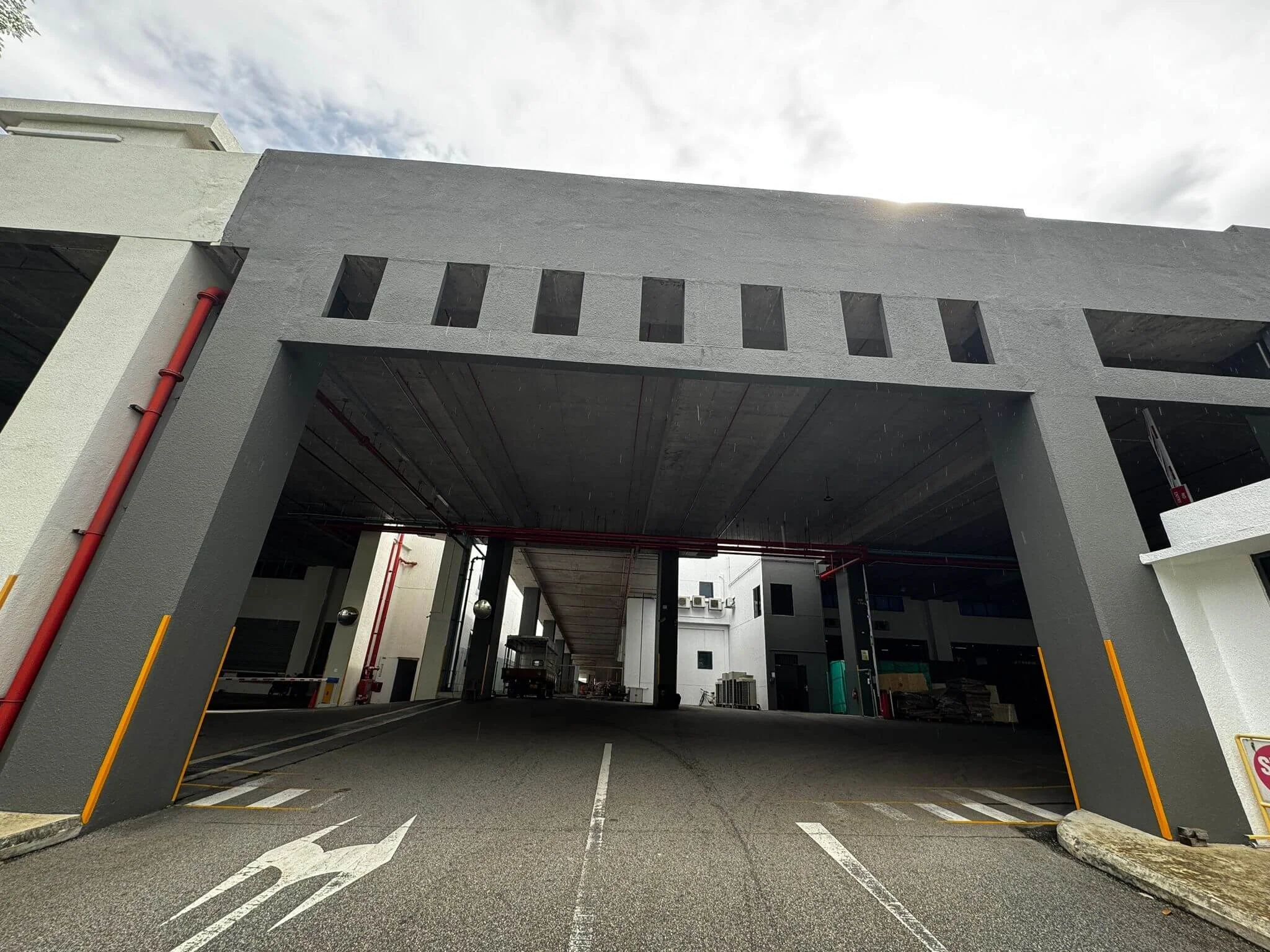 Underground parking garage entrance at a modern building with gray concrete structure, red piping, and a painted arrow on the road.