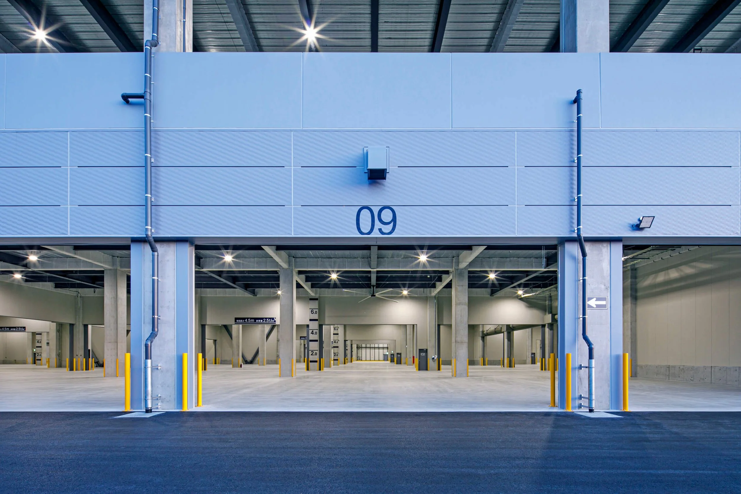 Empty outdoor parking garage with the number 09 on the wall, yellow safety posts, and overhead lighting.