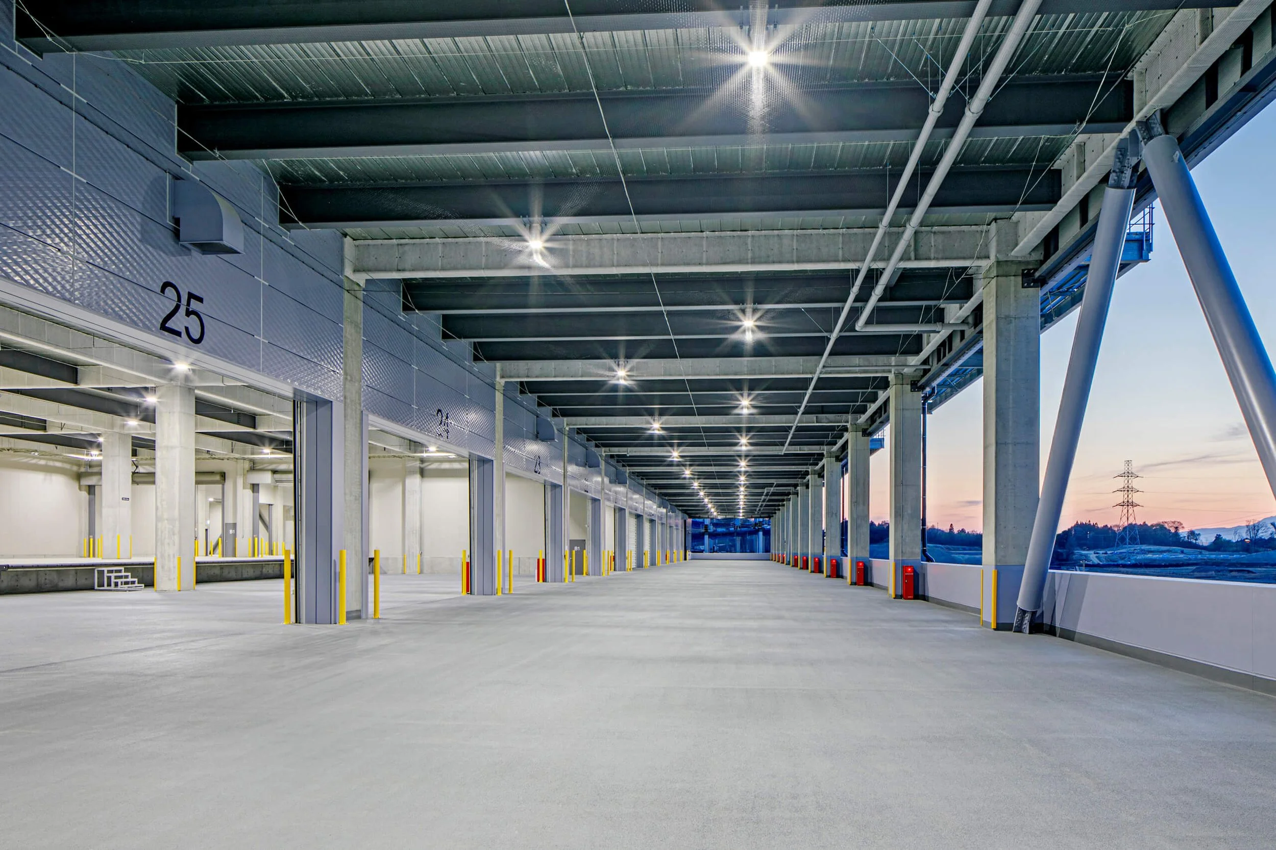 Empty multi-level parking garage with bright ceiling lights and a view of sunset outside