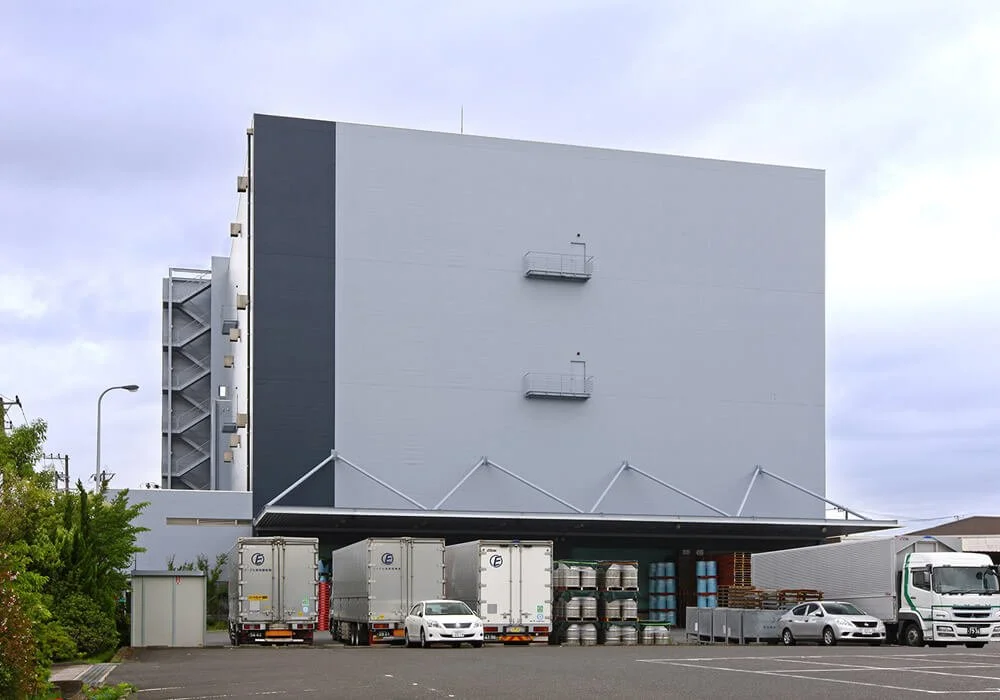 Large industrial building with trucks parked in front, storage tanks, and an outdoor staircase on the side