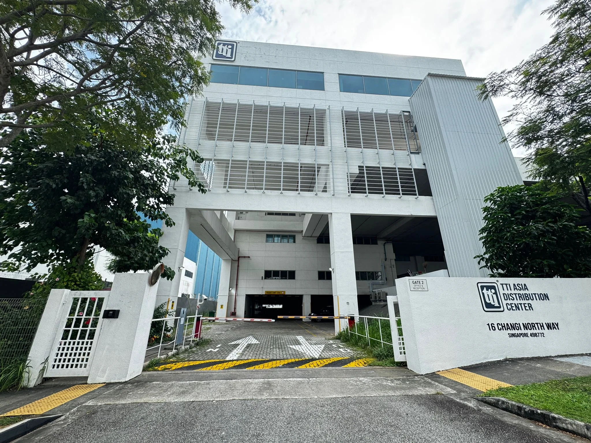Exterior view of the TTI Asia Distribution Center building at 16 Changi North Way, Singapore, showing the entrance with gated security, signage, and trees around the building.