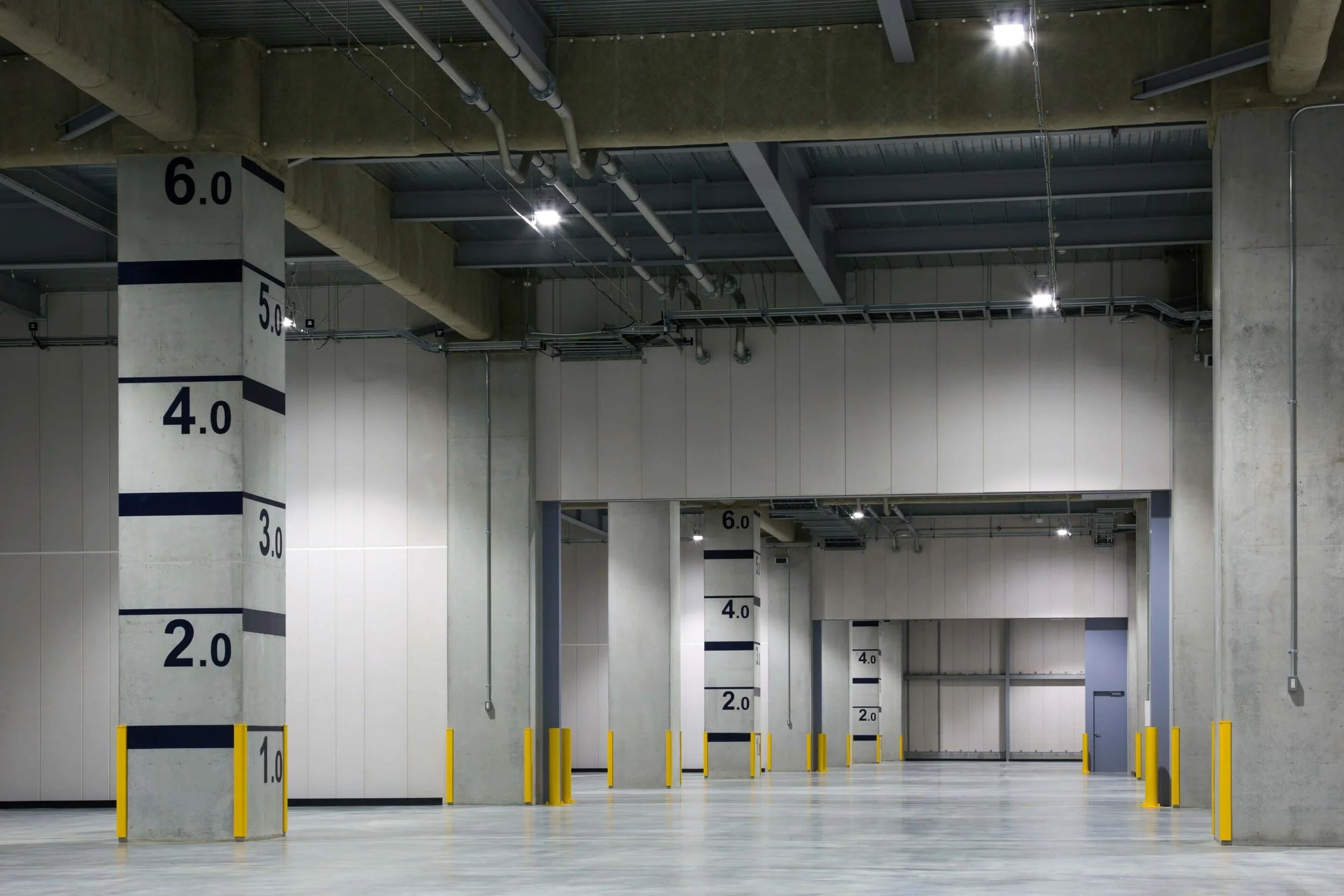 Empty underground parking garage with concrete pillars marked with height restrictions and yellow safety barriers.