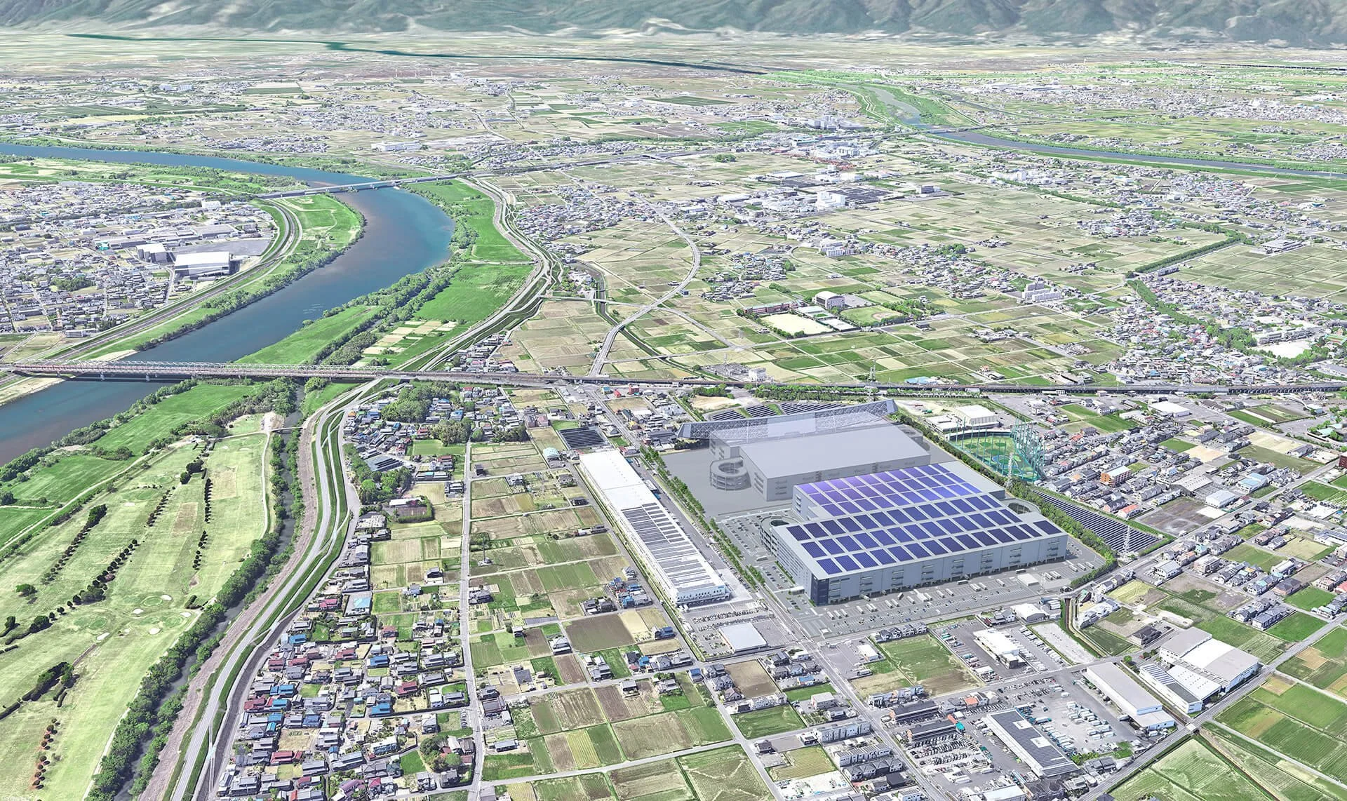 Aerial view of a city with a river, green fields, bridges, and a large complex with solar panels on the roof.