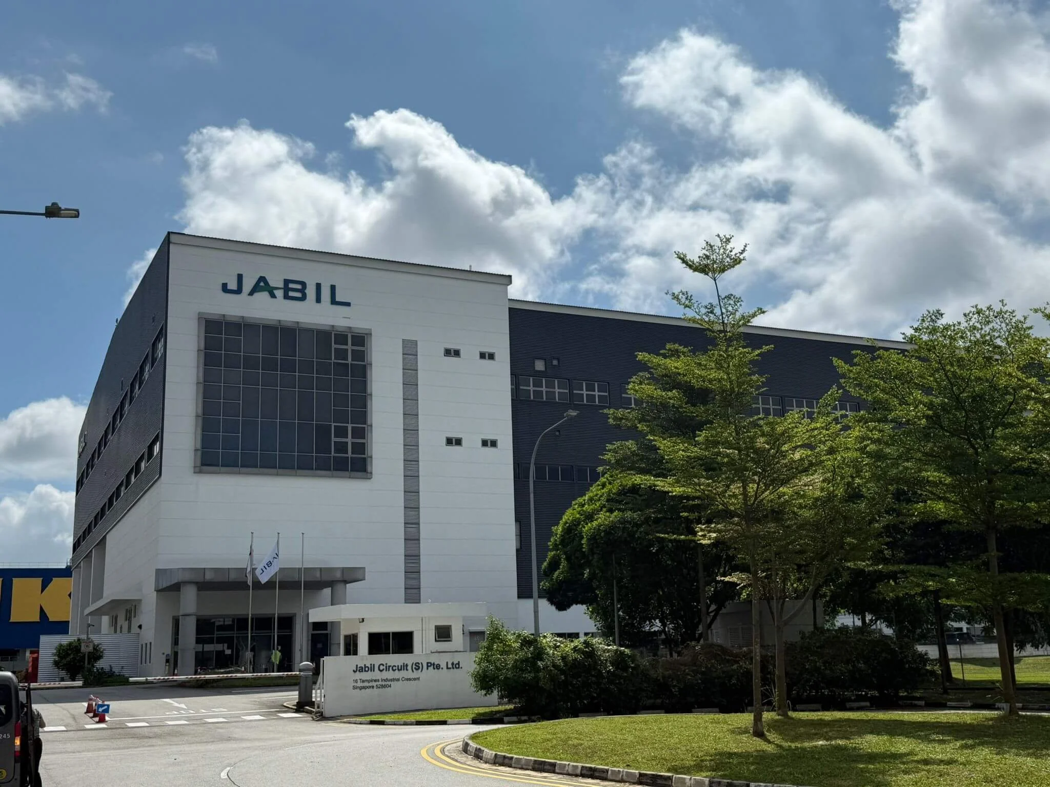 Modern black and white office building with the sign 'JABIL' on the facade, surrounded by greenery and a partly cloudy sky.